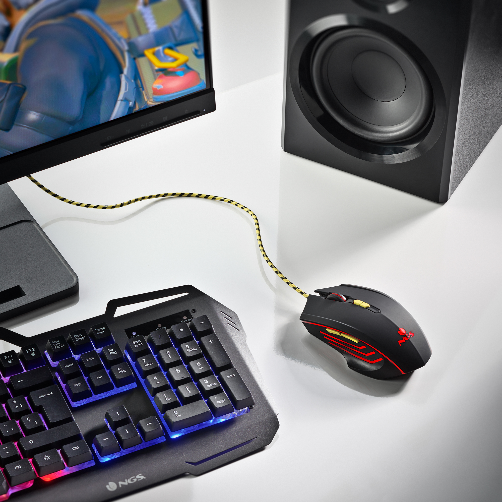 Configuración de escritorio con teclado, ratón y monitor. Teclado con luces RGB. Altavoz negro visible.