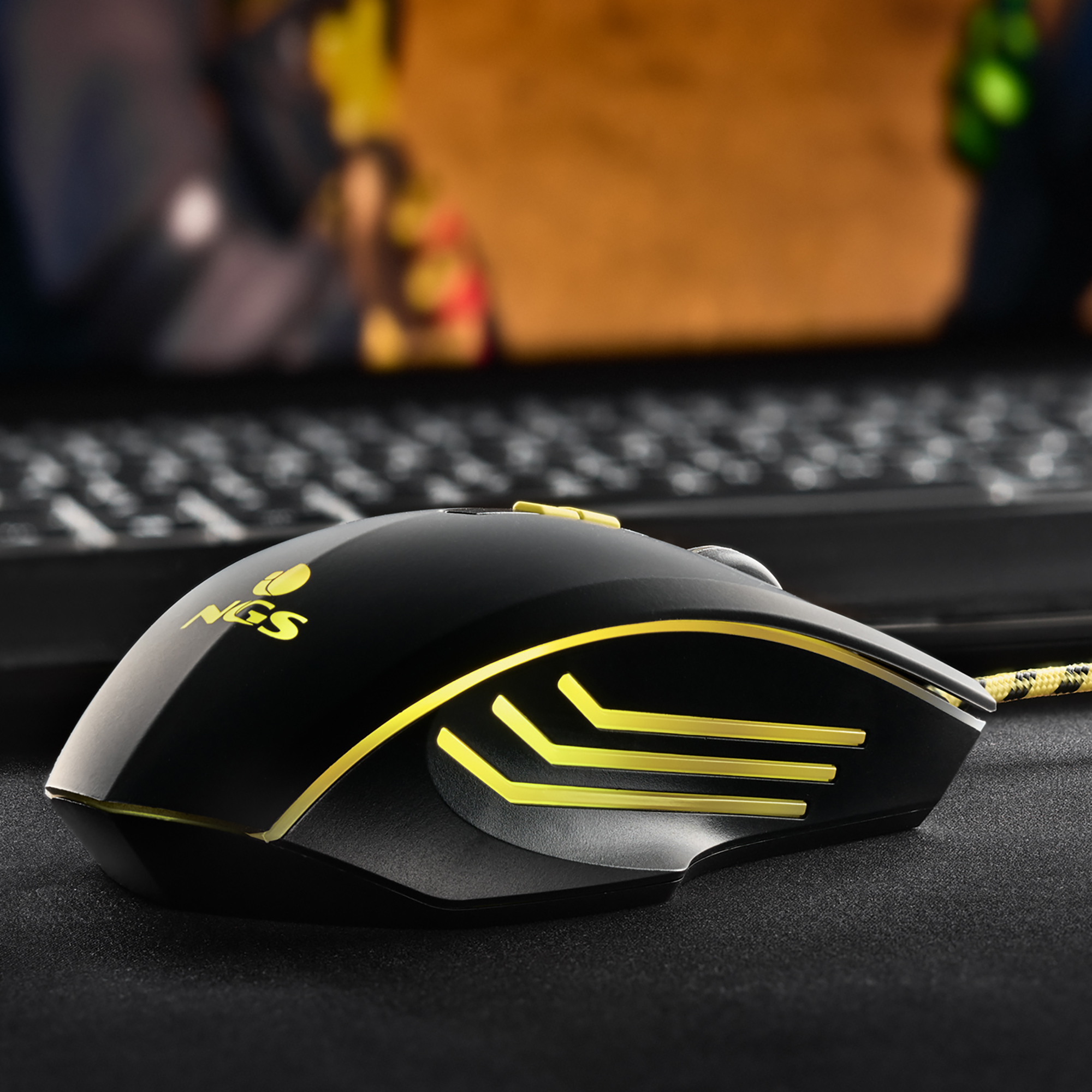 Ratón gaming negro con detalles amarillos, sobre una alfombrilla negra.
