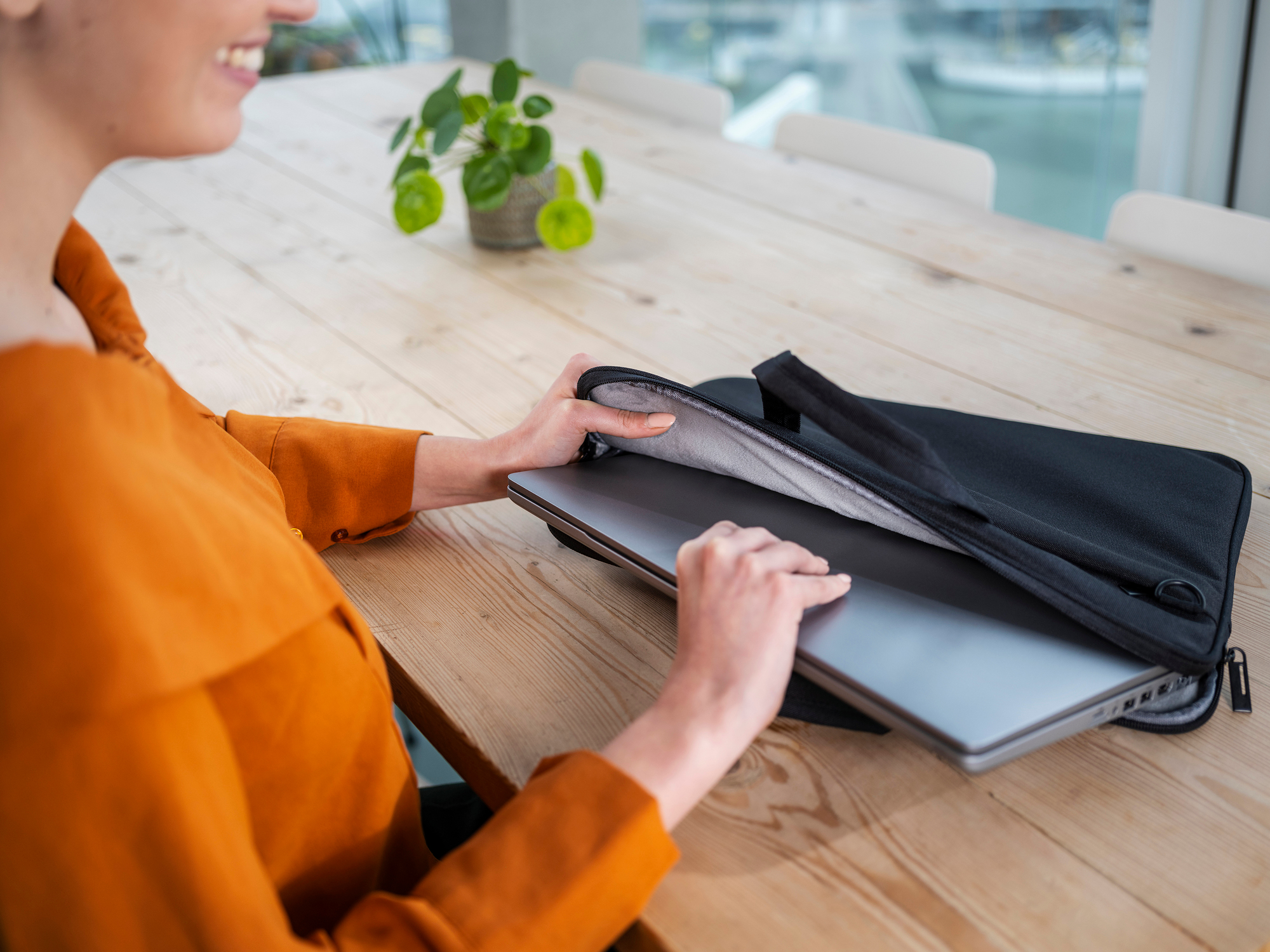 Woman putting a laptop into a black laptop bag on a wooden table.