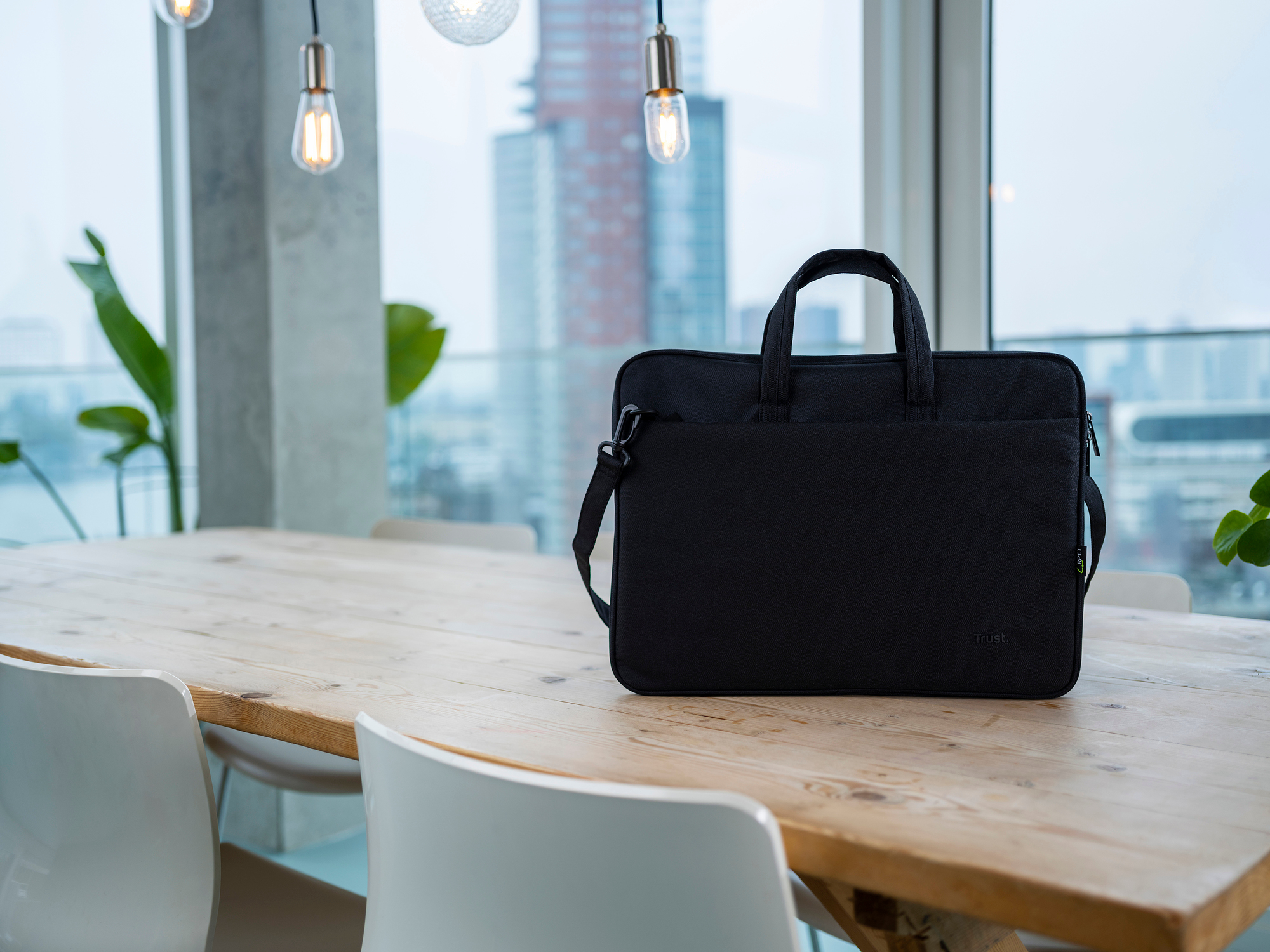 Black laptop bag on a wooden table in front of a window with city view.