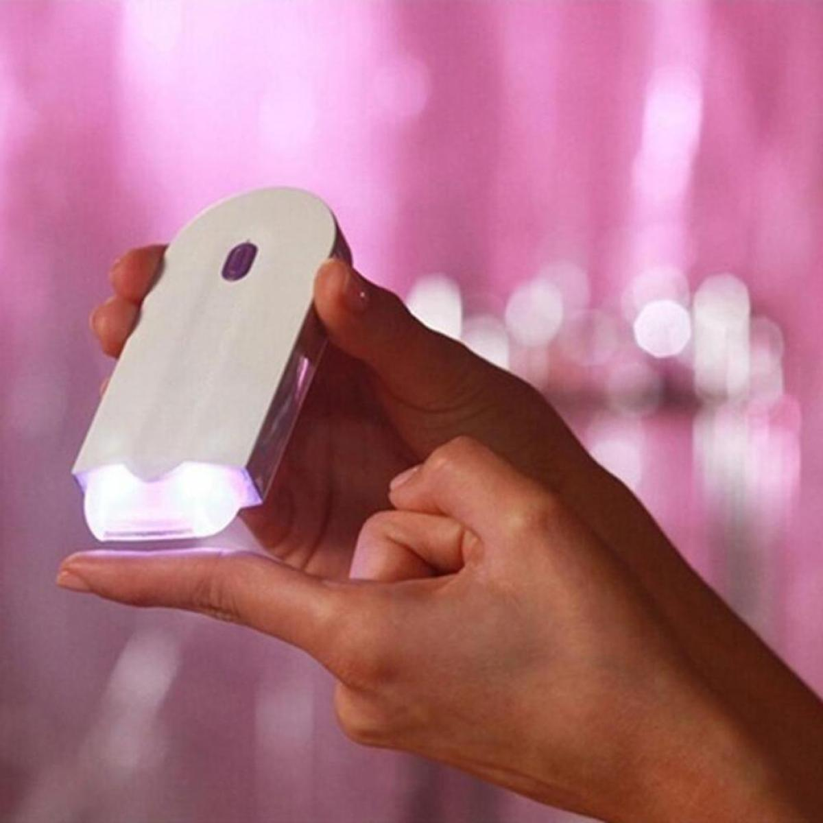 Eine Hand hält ein weißes Gerät mit Licht. Ein rosa Hintergrund ist sichtbar.