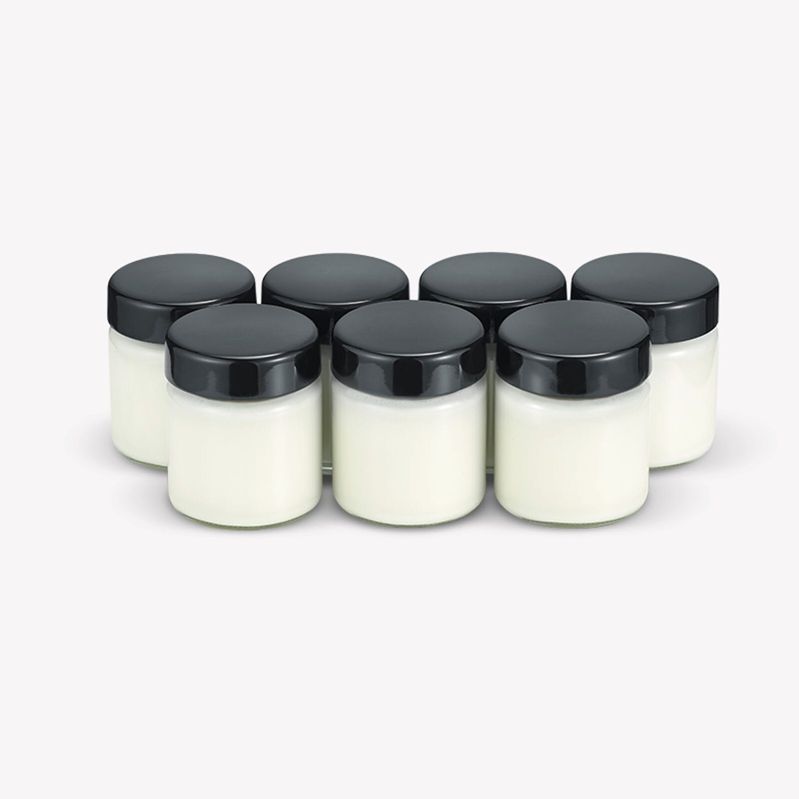 Seis tarros pequeños con tapas negras, llenos de crema blanca.