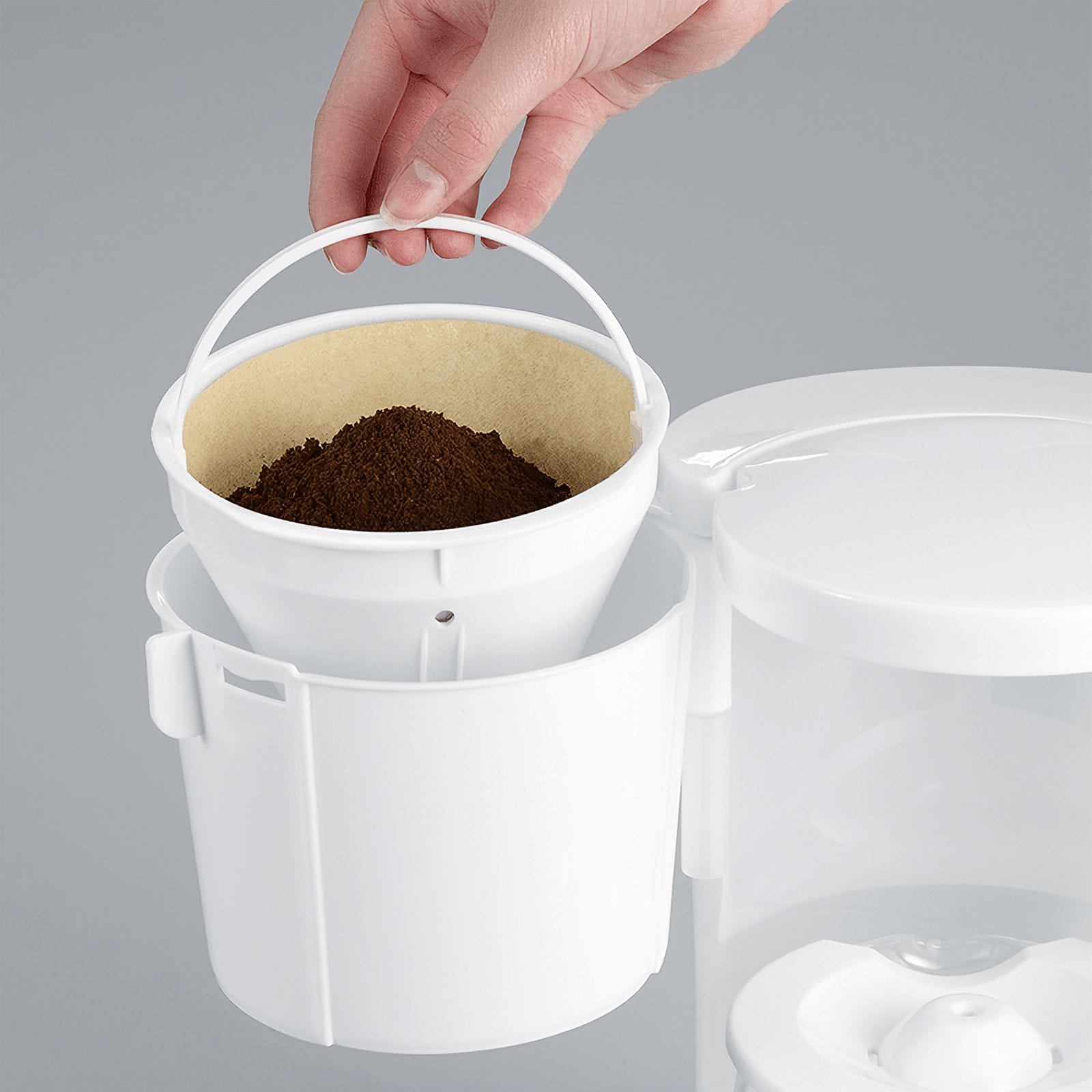 Una mano versa caffè macinato in un filtro di carta posto in una macchina per il caffè bianca.