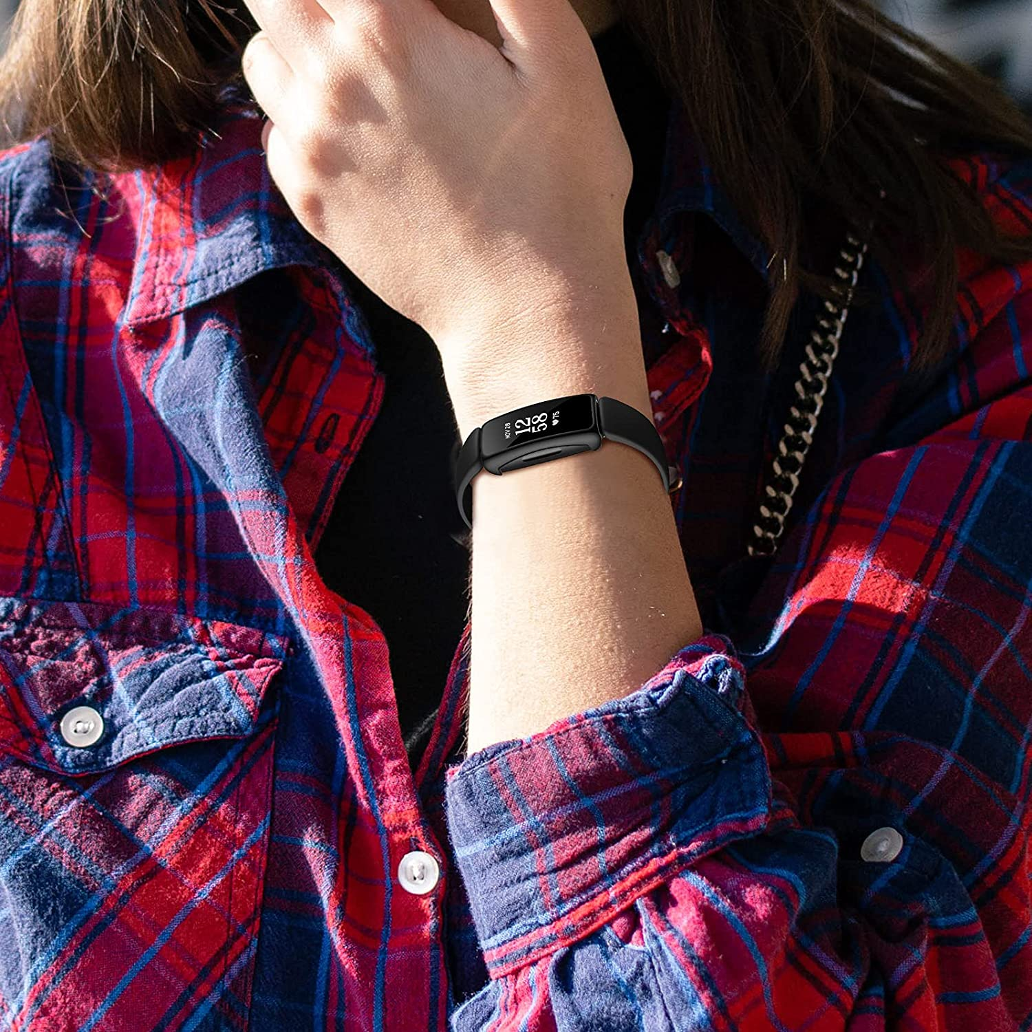 Handgelenk mit schwarzem Fitnesstracker. Person trägt rot-blaues Karohemd.
