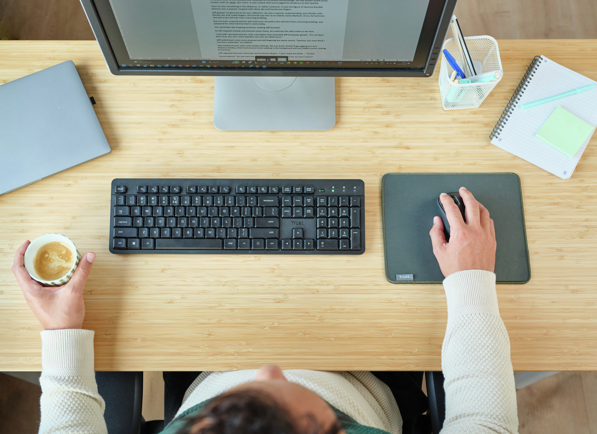 Widok z góry na osobę przy biurku z komputerem, klawiaturą i filiżanką kawy.