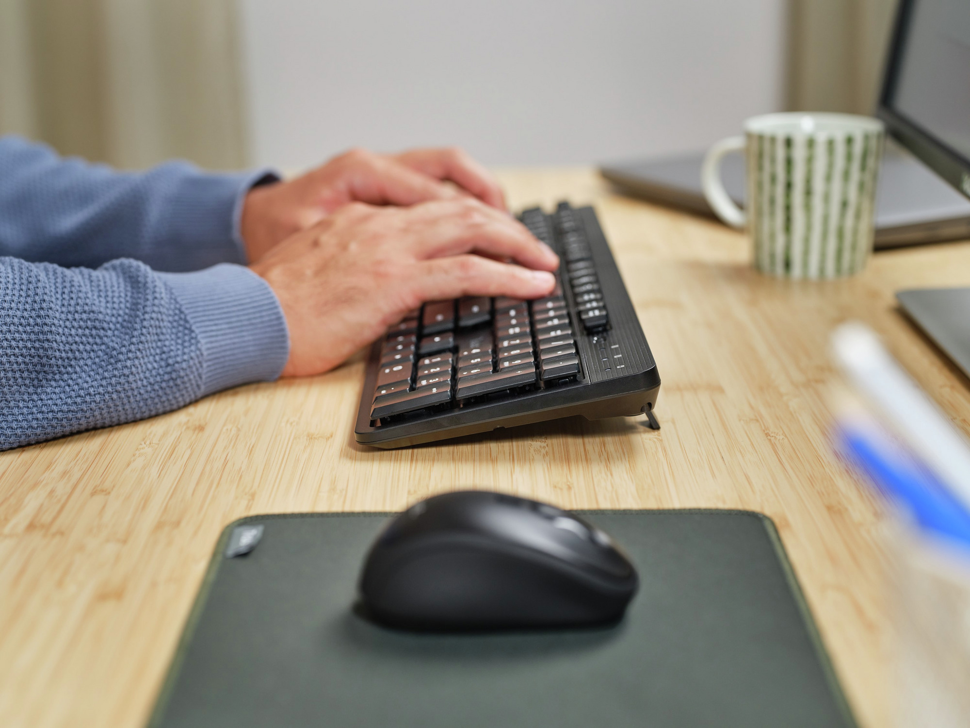 Ręce piszące na czarnej klawiaturze, z myszą i biurkiem, z niskiego kąta.