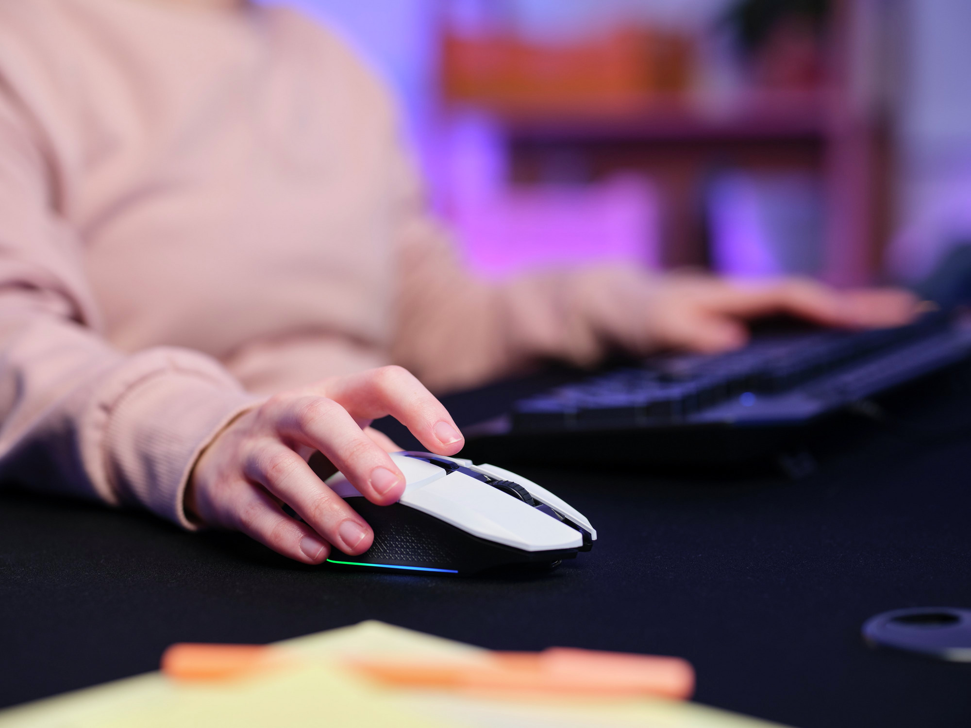 Eine Hand benutzt eine weiß-schwarze Gaming-Maus auf einem schwarzen Schreibtisch, im Hintergrund eine Tastatur.