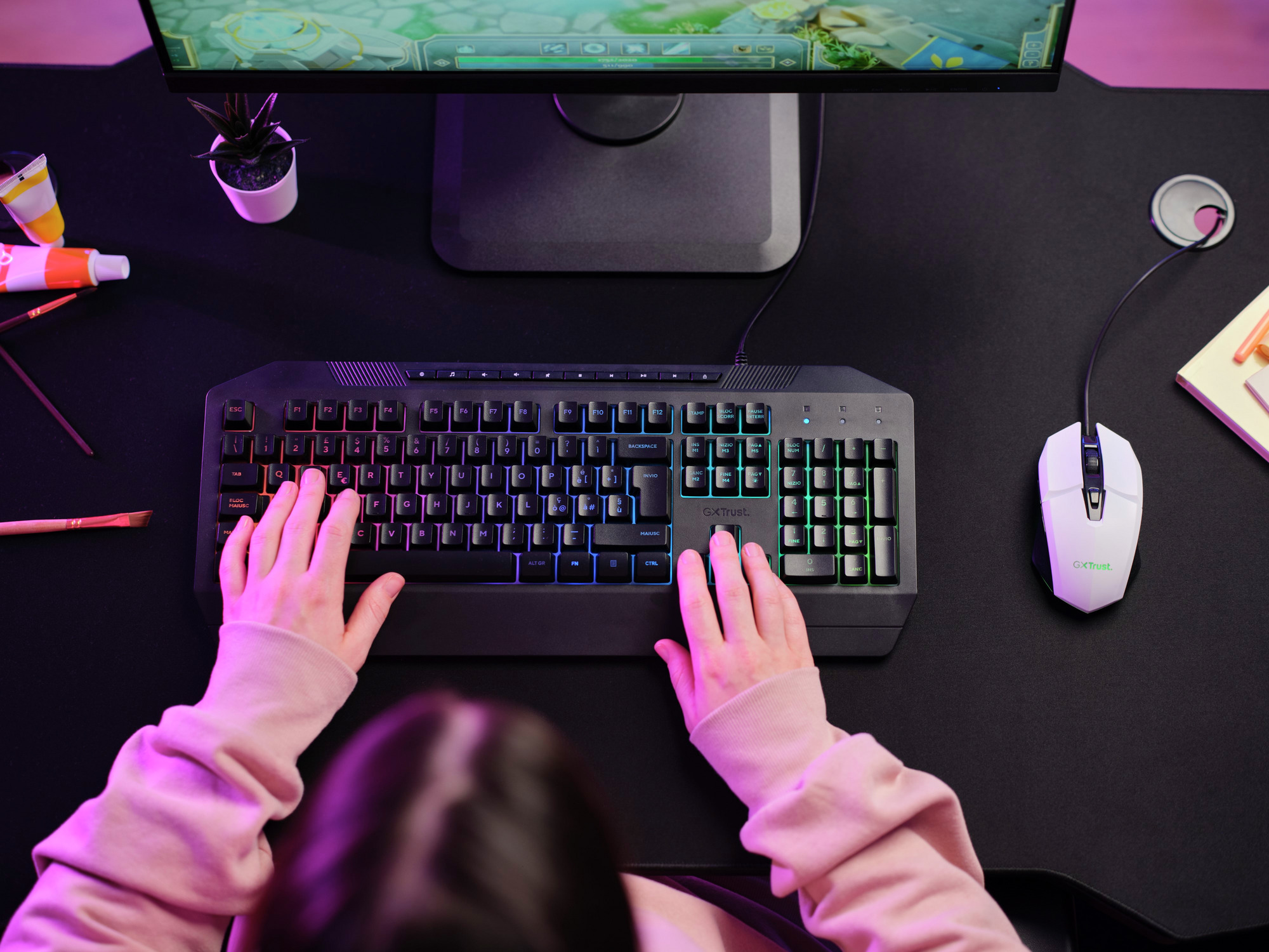 Dłonie piszące na klawiaturze z kolorowymi światłami. Mysz po prawej, widoczny monitor.
