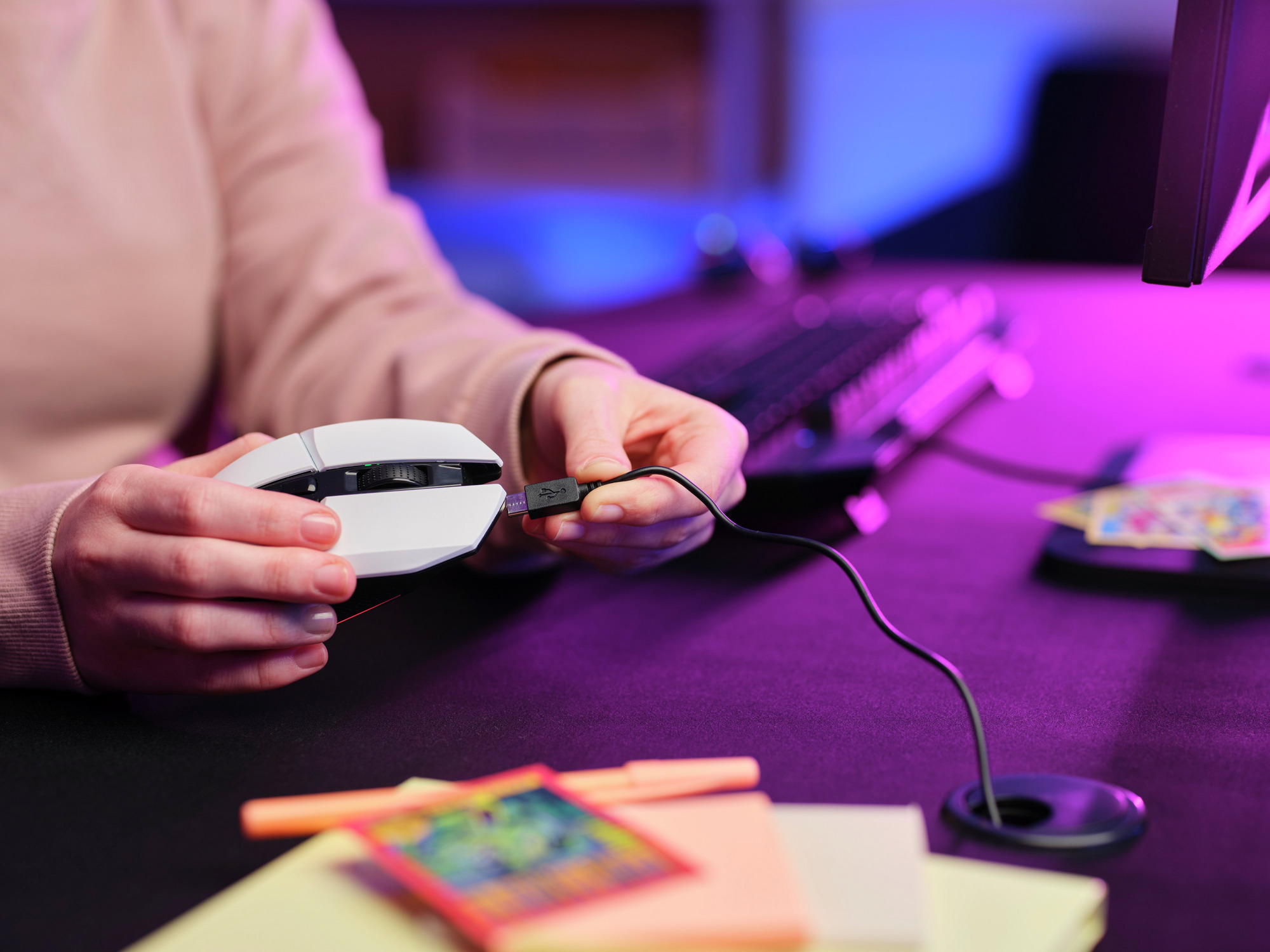 Person schließt eine weiße Gaming-Maus an einen Monitor an. Schreibtisch mit Tastatur und Haftnotizen.