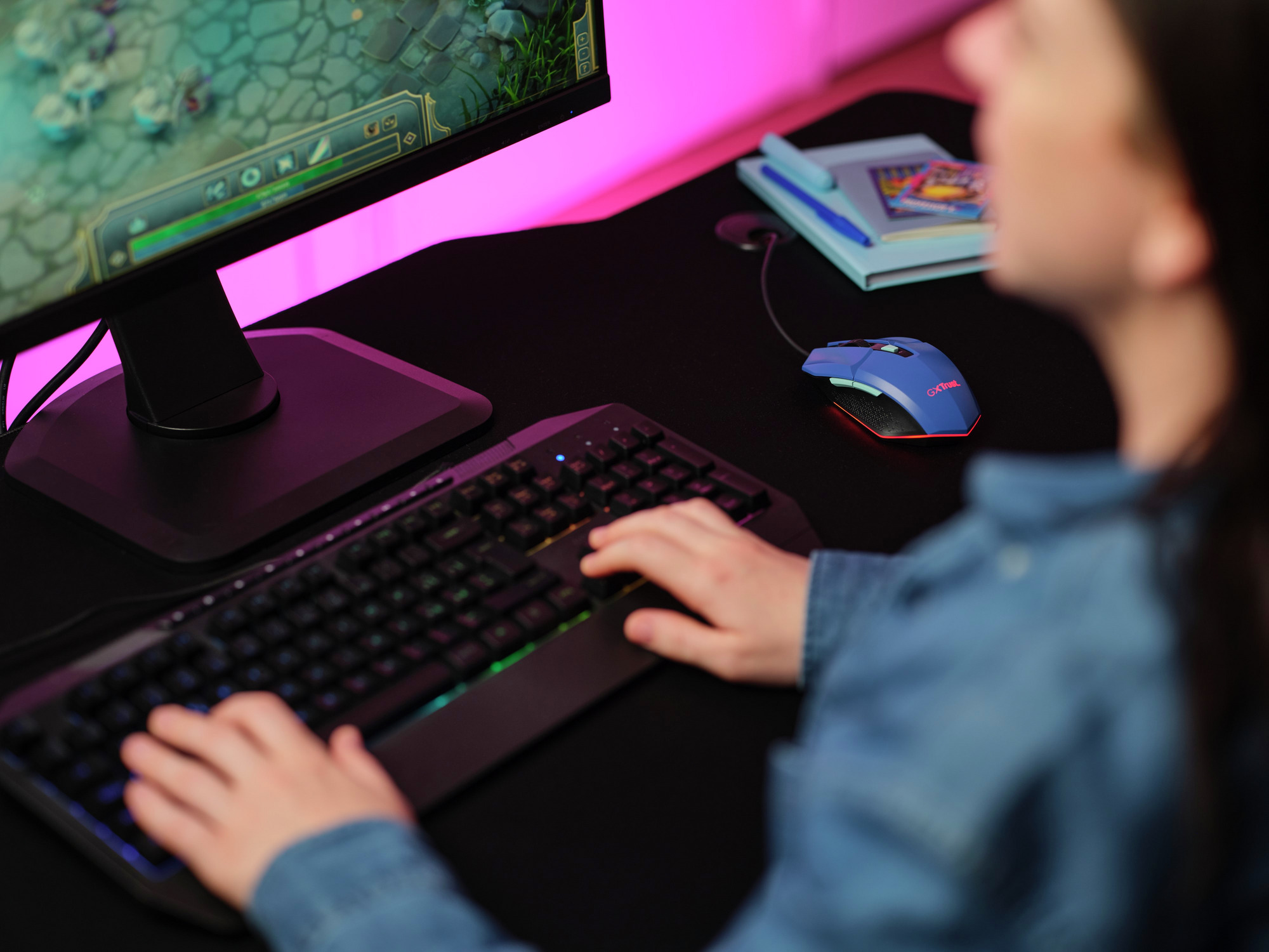 Osoba grająca na klawiaturze i myszy. Monitor wyświetla grę. Różowe światło za monitorem.