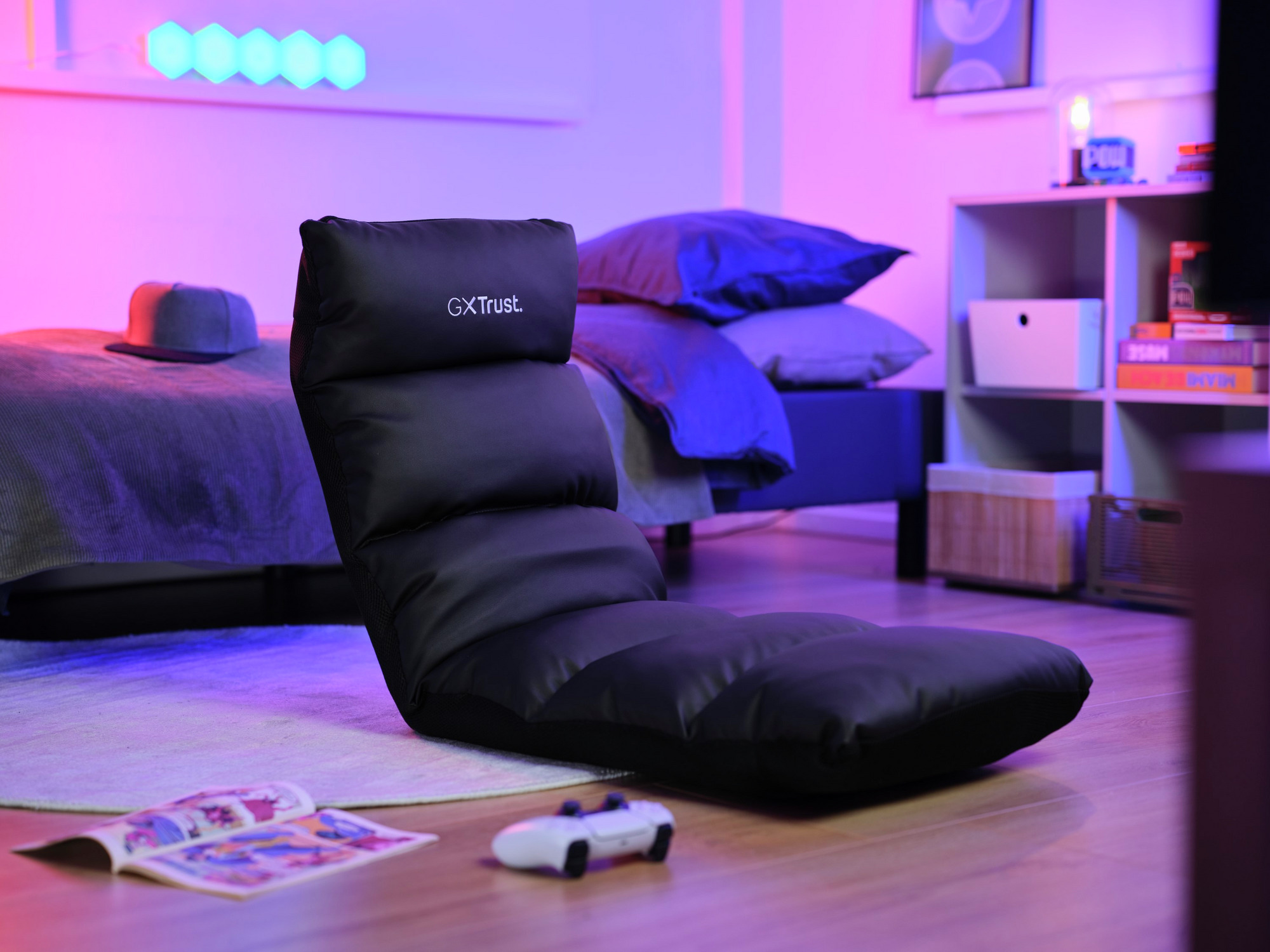 Czarny fotel podłogowy w pokoju z łóżkiem, kapeluszem i kontrolerem. Różowe i niebieskie światła.