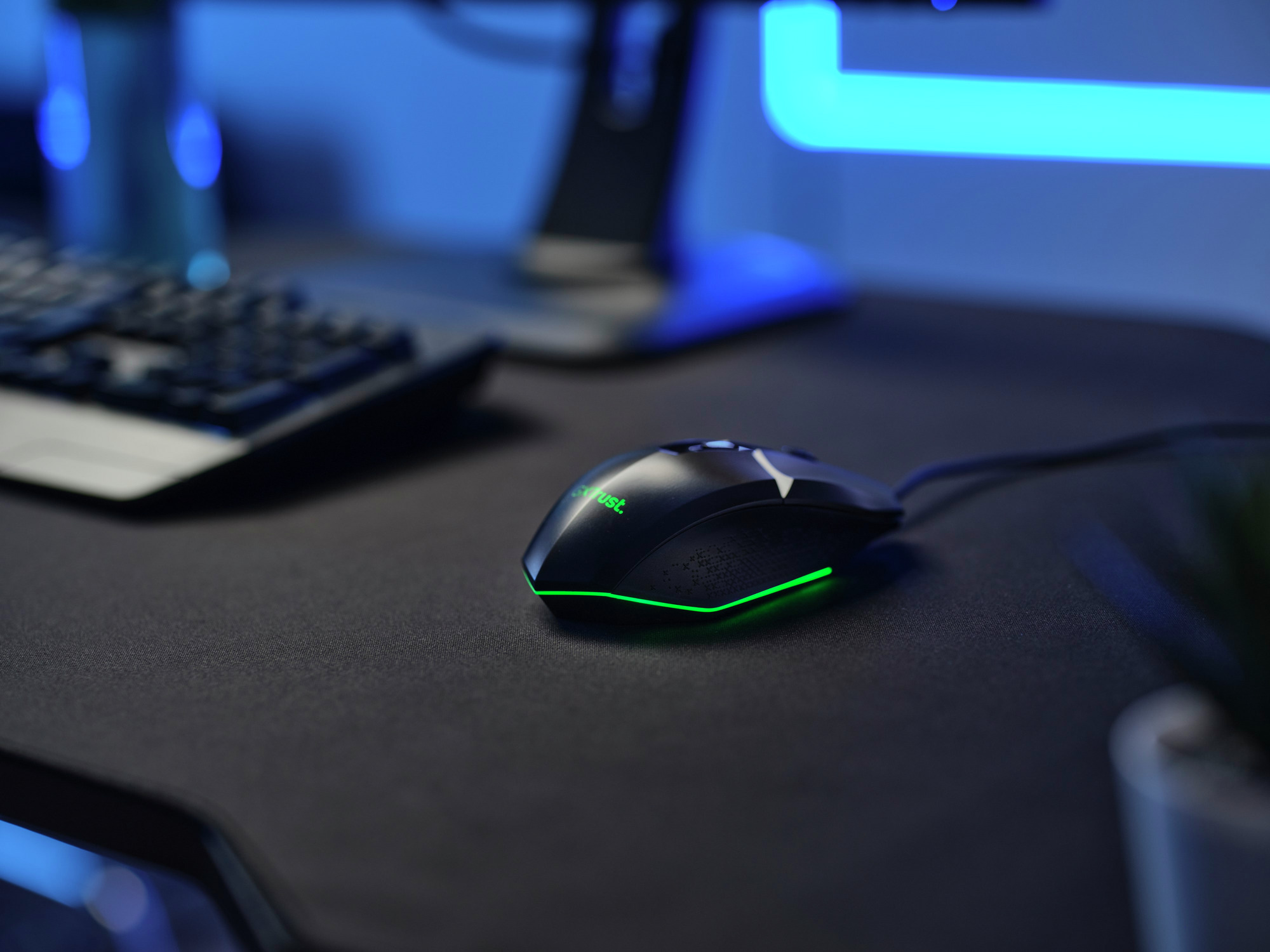 Schwarze Gaming-Maus mit grünen Akzenten auf einem schwarzen Schreibtisch. Hintergrund: Monitor.