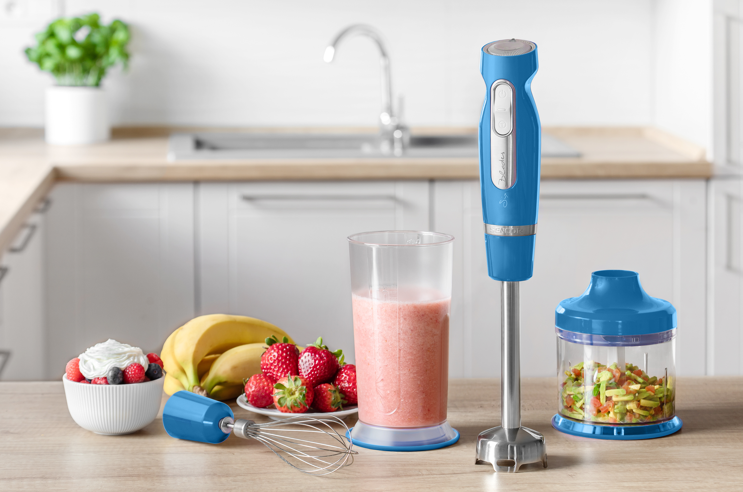 Niebieski blender ręczny z akcesoriami, koktajle i owoce na drewnianym blacie kuchennym.