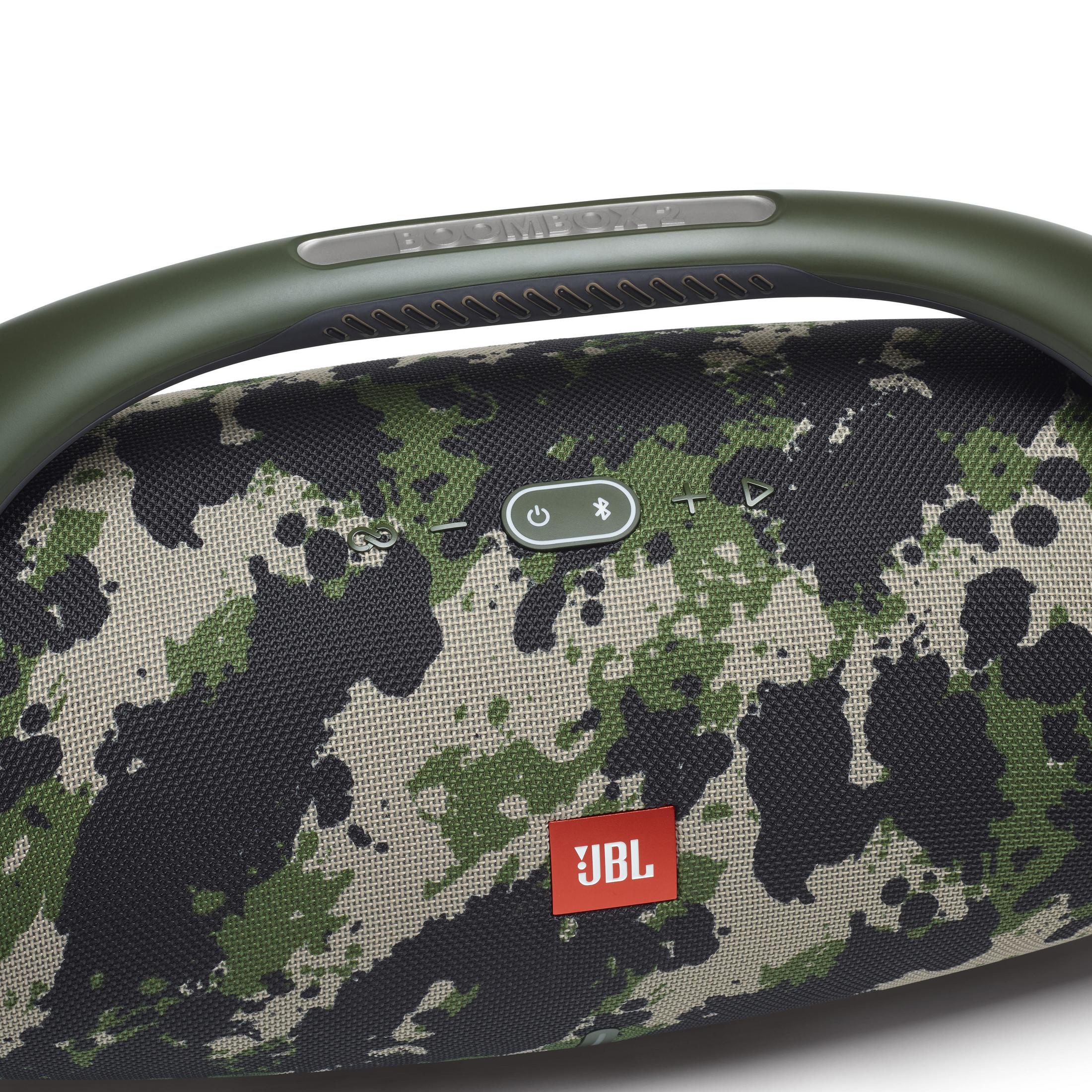 Tarnfarbener JBL Boombox-Lautsprecher mit olivgrünem Griff, auf weißem Hintergrund.