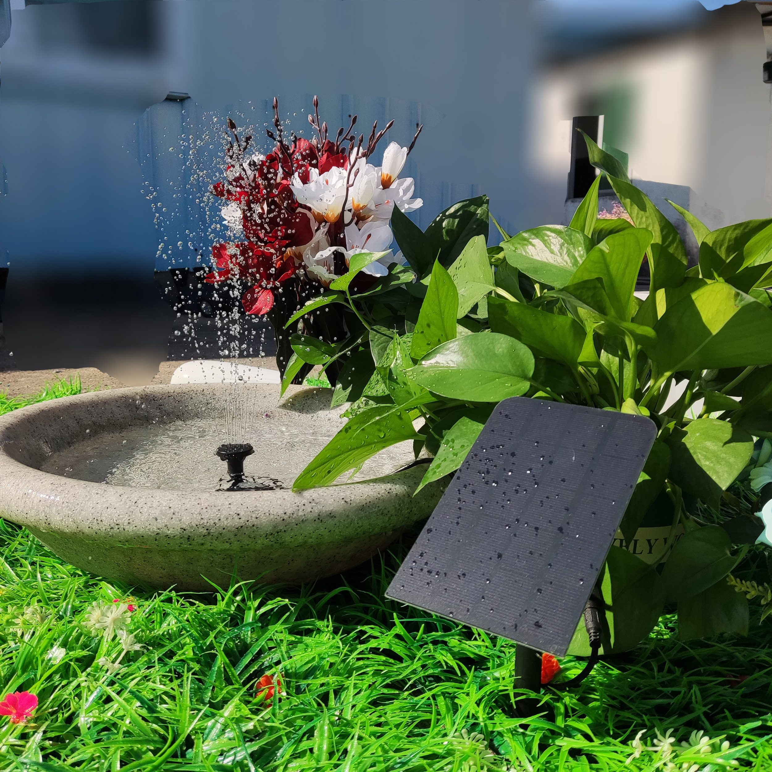 Ein Springbrunnen mit Blumen und einem Solarpanel in einem grasbewachsenen Bereich.