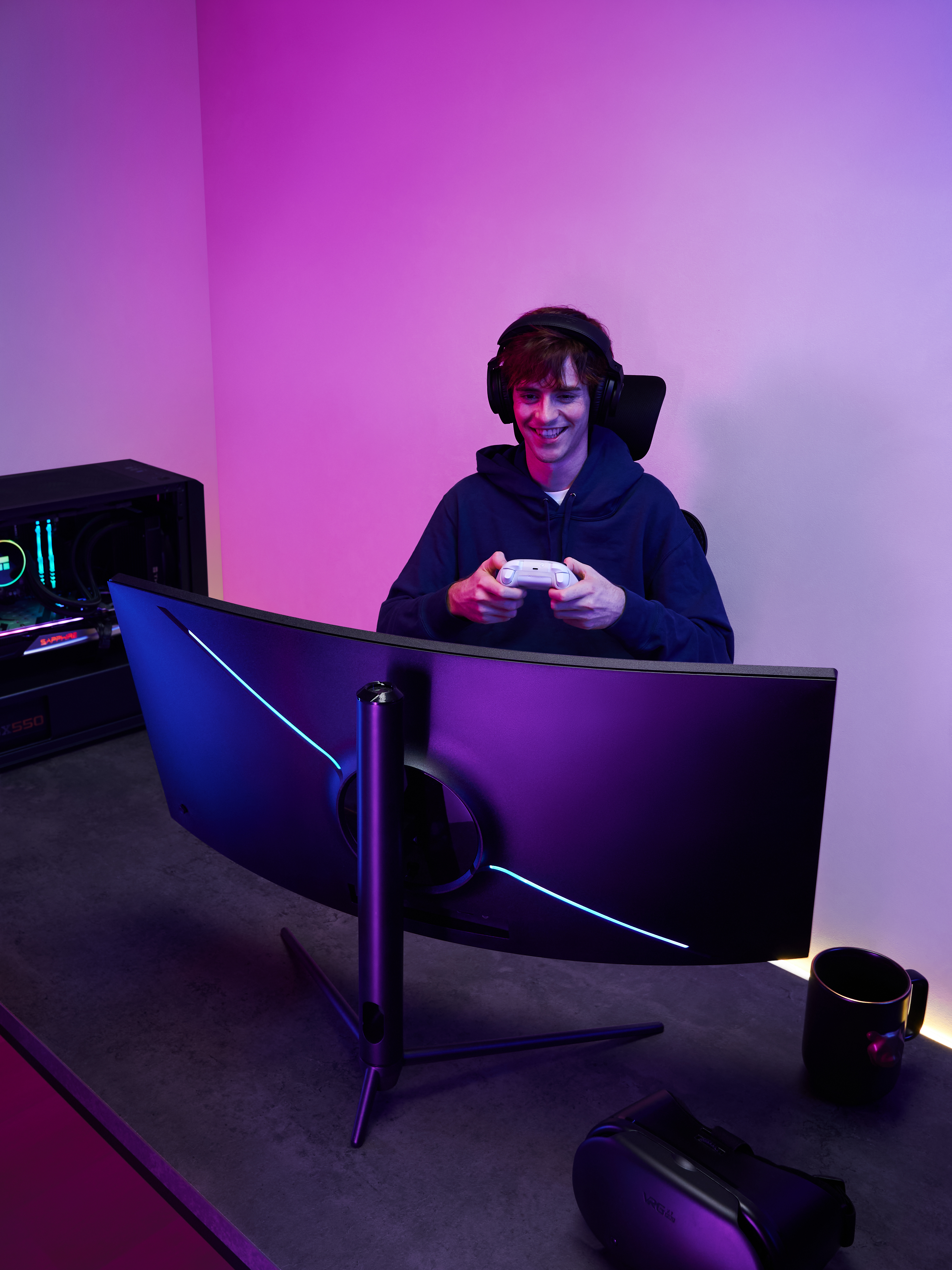 Mężczyzna gra w grę na zakrzywionym monitorze do gier w słuchawkach. Pokój ma fioletowe i niebieskie światła.