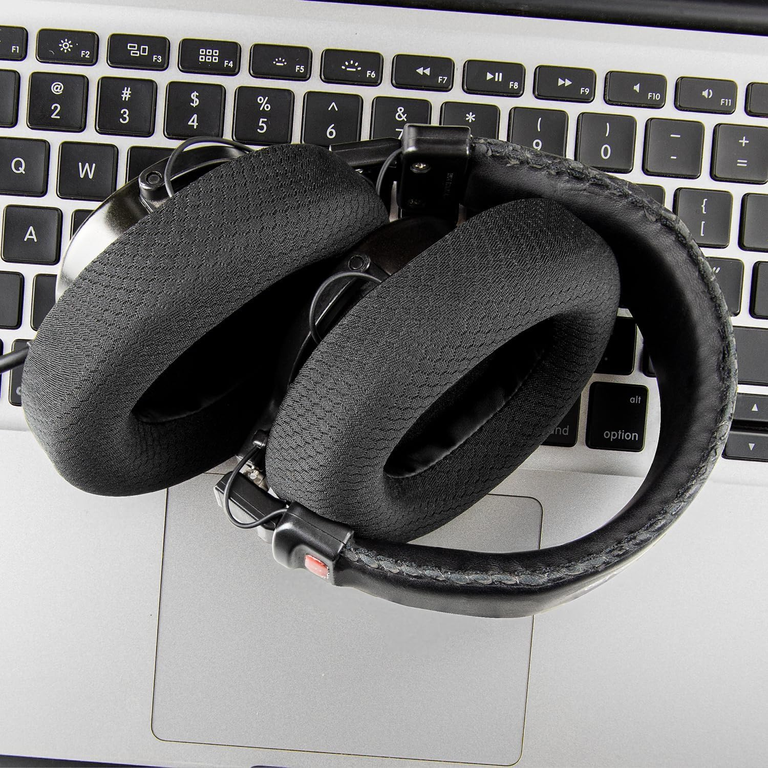 Cuffie nere piegate su una tastiera di un laptop con superficie argentata.