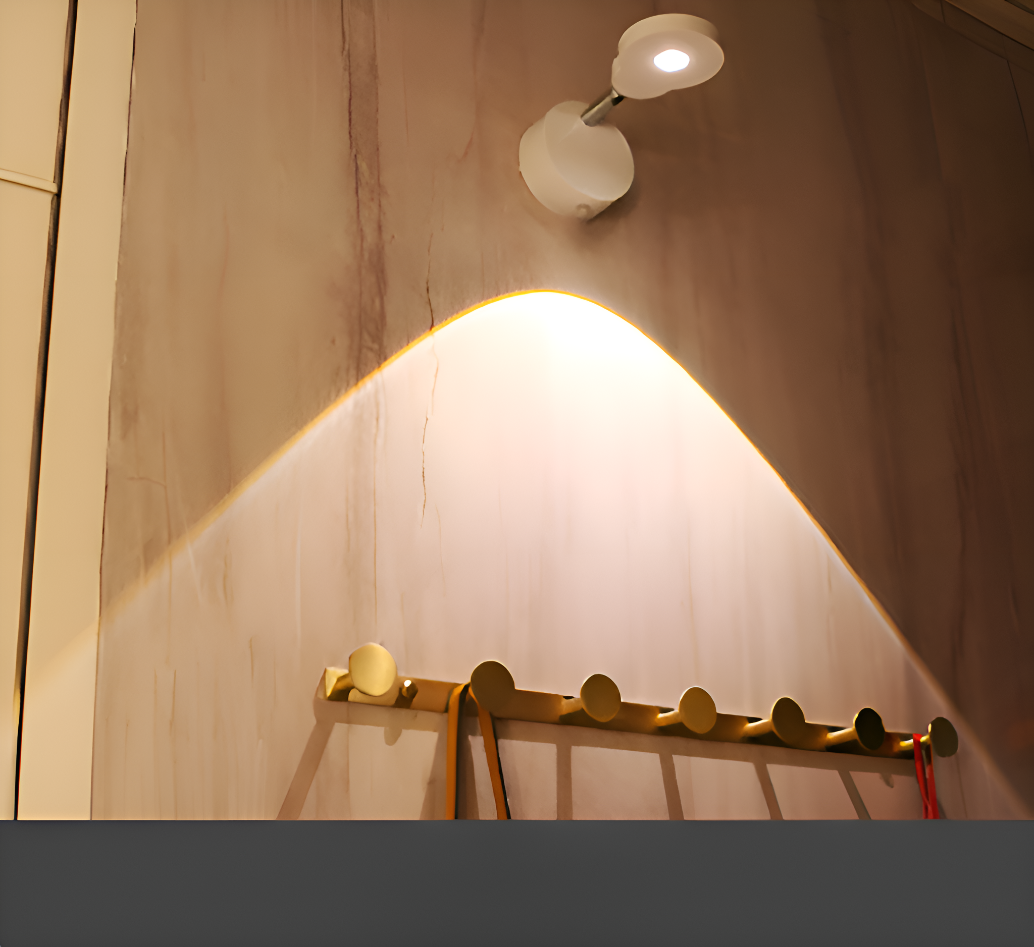 Wand mit einer Leuchte und einer Garderobe. Das Licht wirft einen warmen Schein auf die Wand.