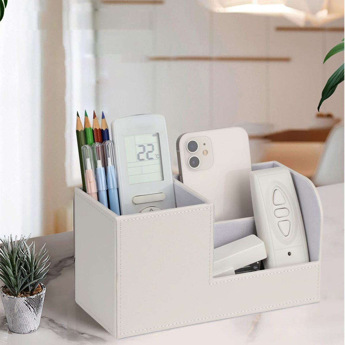 Ein weißer Schreibtisch-Organizer mit Bleistiften, Fernbedienung, Telefon und Hefter.