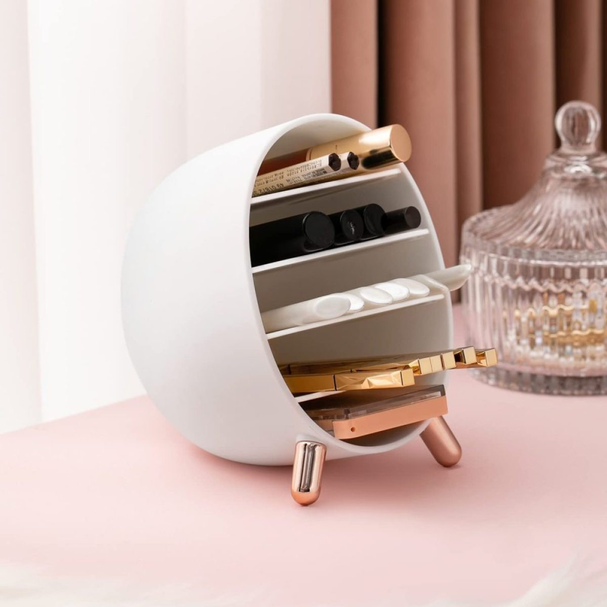 Kosmetik-Organizer mit Make-up darin. Der Organizer ist weiß mit goldenen Beinen.