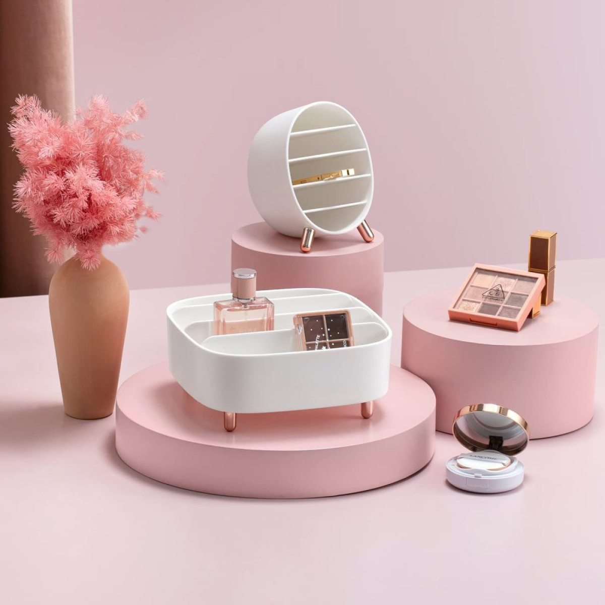 Weißer Kosmetik-Organizer mit Kosmetika, Parfüm und dekorativen rosa Blumen auf rosa Podesten.