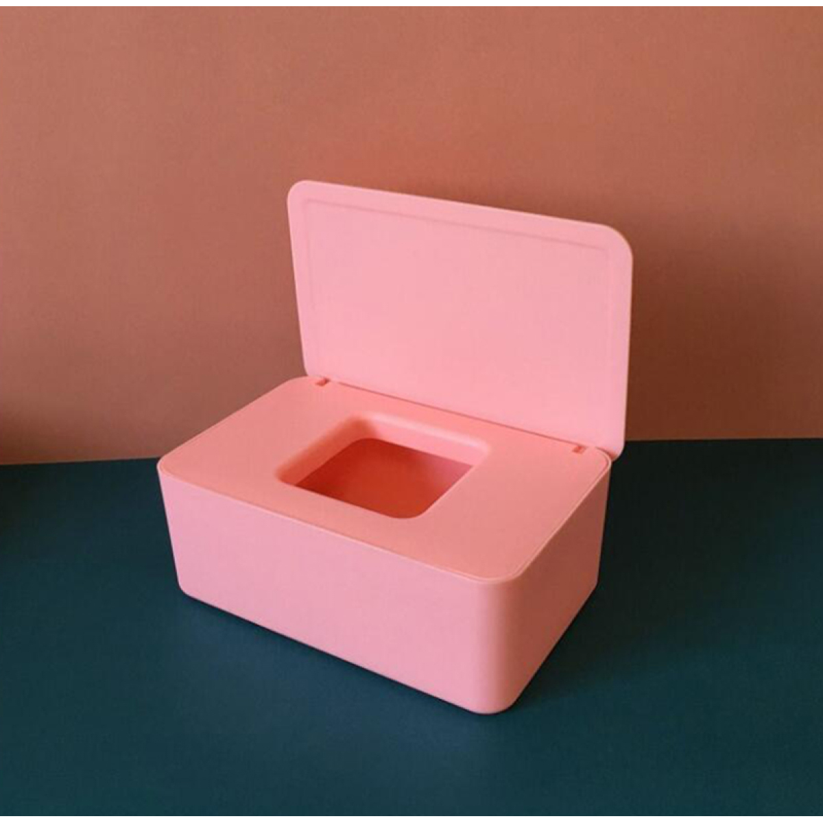 Rosa rechteckige Taschentuchbox mit offenem Deckel, auf blaugrüner Oberfläche.