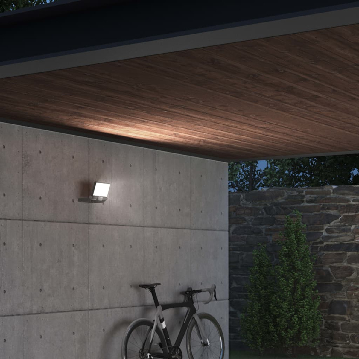 Eine moderne Außenwandleuchte an einer Betonwand unter einer Holzdecke. Ein Fahrrad steht darunter.