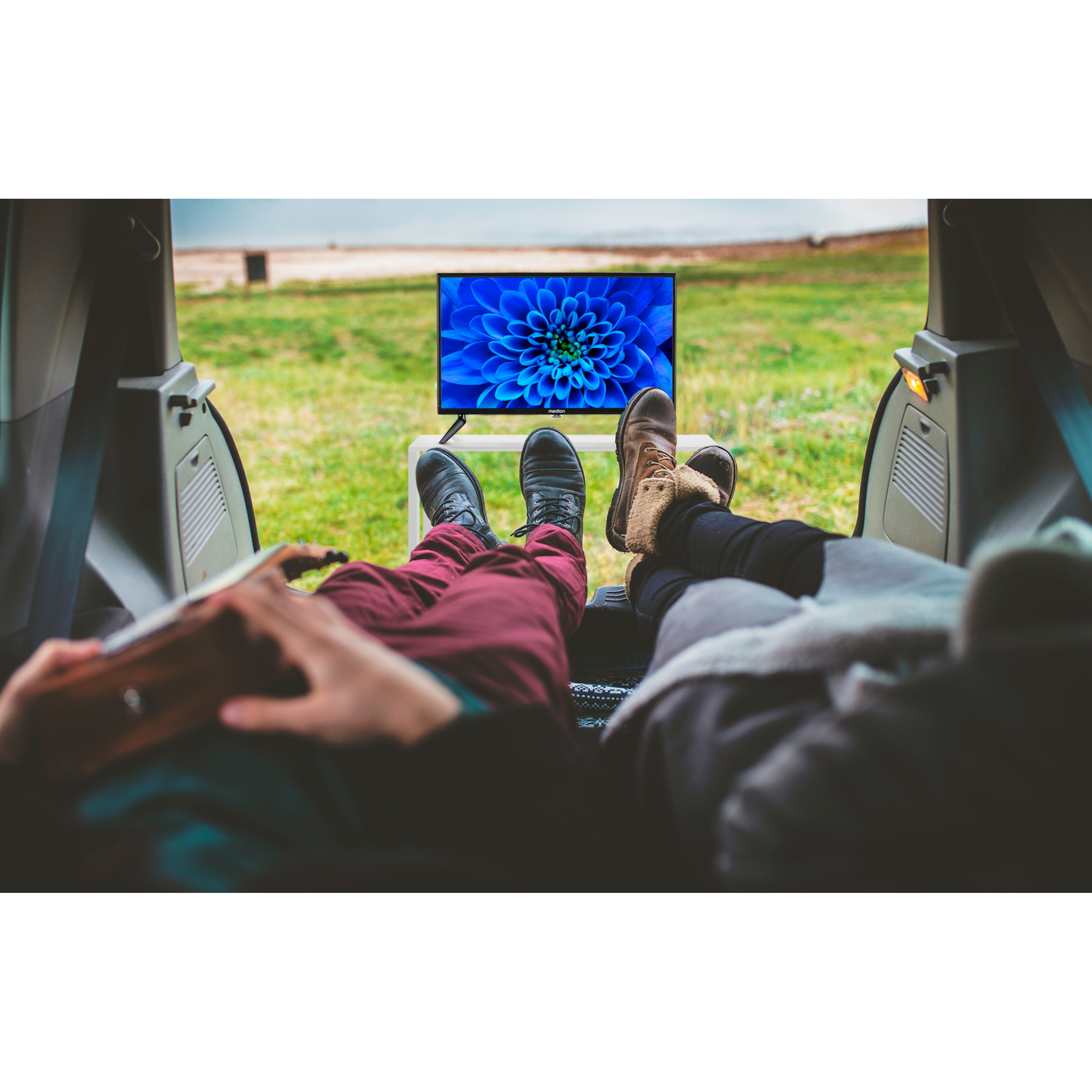 Twee mensen in een auto kijken tv. Voeten en benen zichtbaar; blauw bloemenscherm.