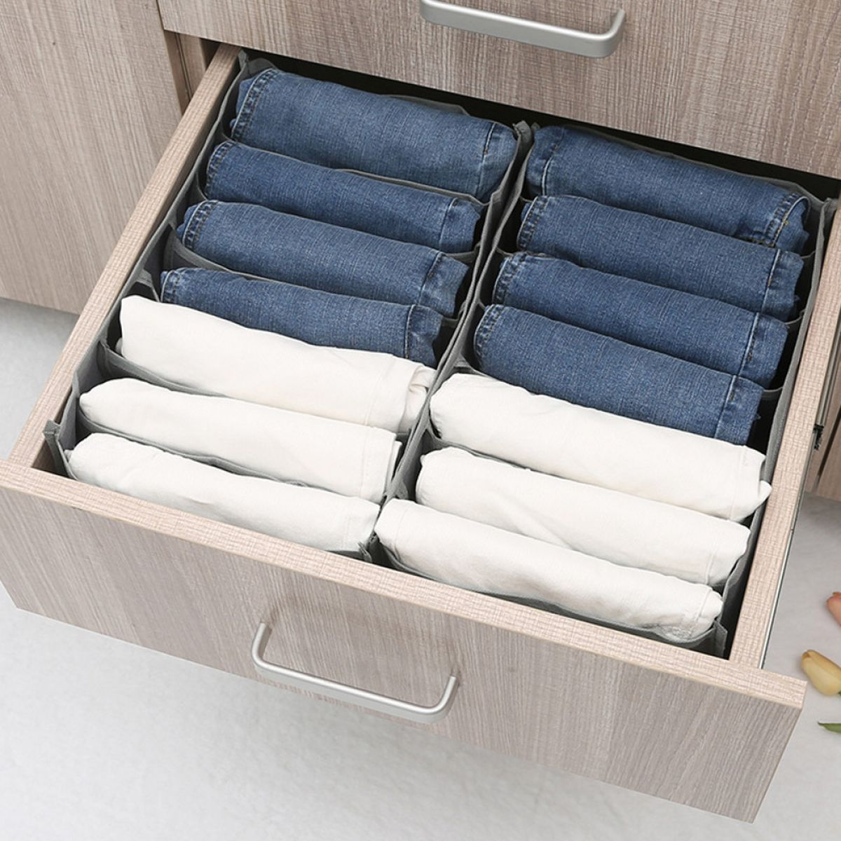 Eine Schublade mit gefalteten Jeans und weißen Hemden, ordentlich in Fächern organisiert.