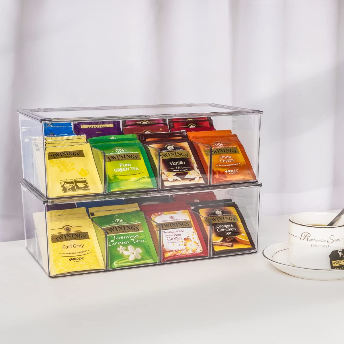 Zwei transparente Tee-Organizer mit Twinings Teebeuteln. Rechts ein Becher mit Untertasse.