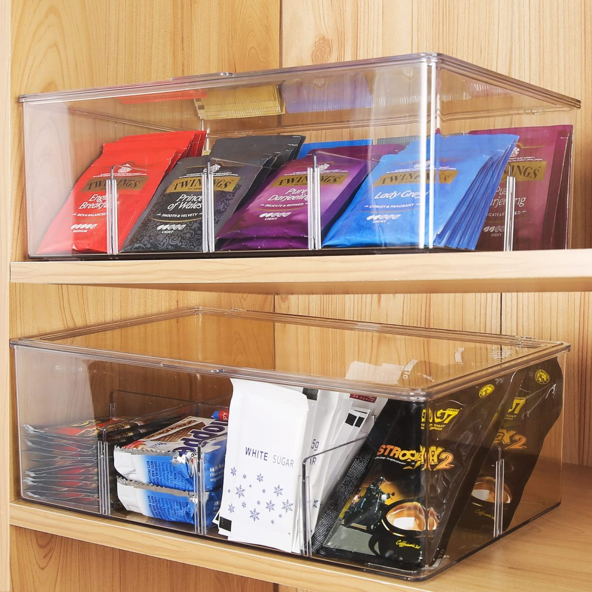 Zwei transparente Boxen mit Teebeuteln und Snacks darin, auf einem Holzregal.