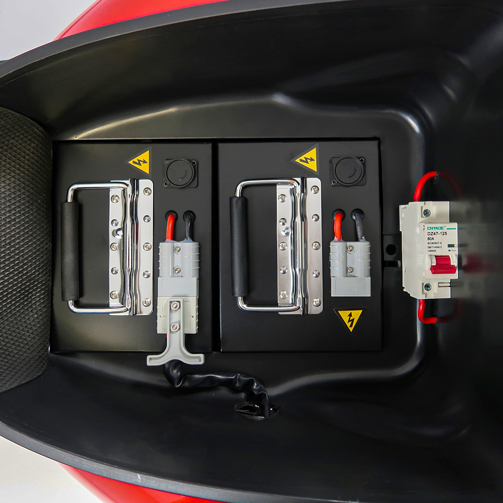 Offenes Fach eines roten Rollers, zeigt schwarze Behälter mit elektrischen Komponenten und Verkabelung.