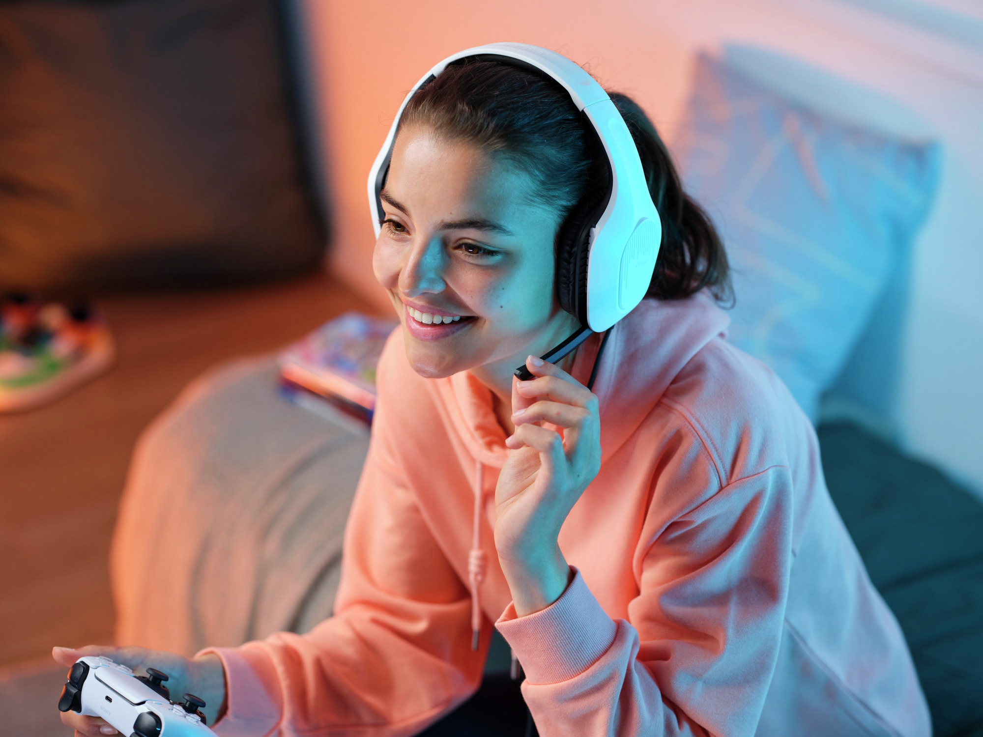 Młoda kobieta w słuchawkach i bluzie z kapturem uśmiecha się, trzymając kontroler.