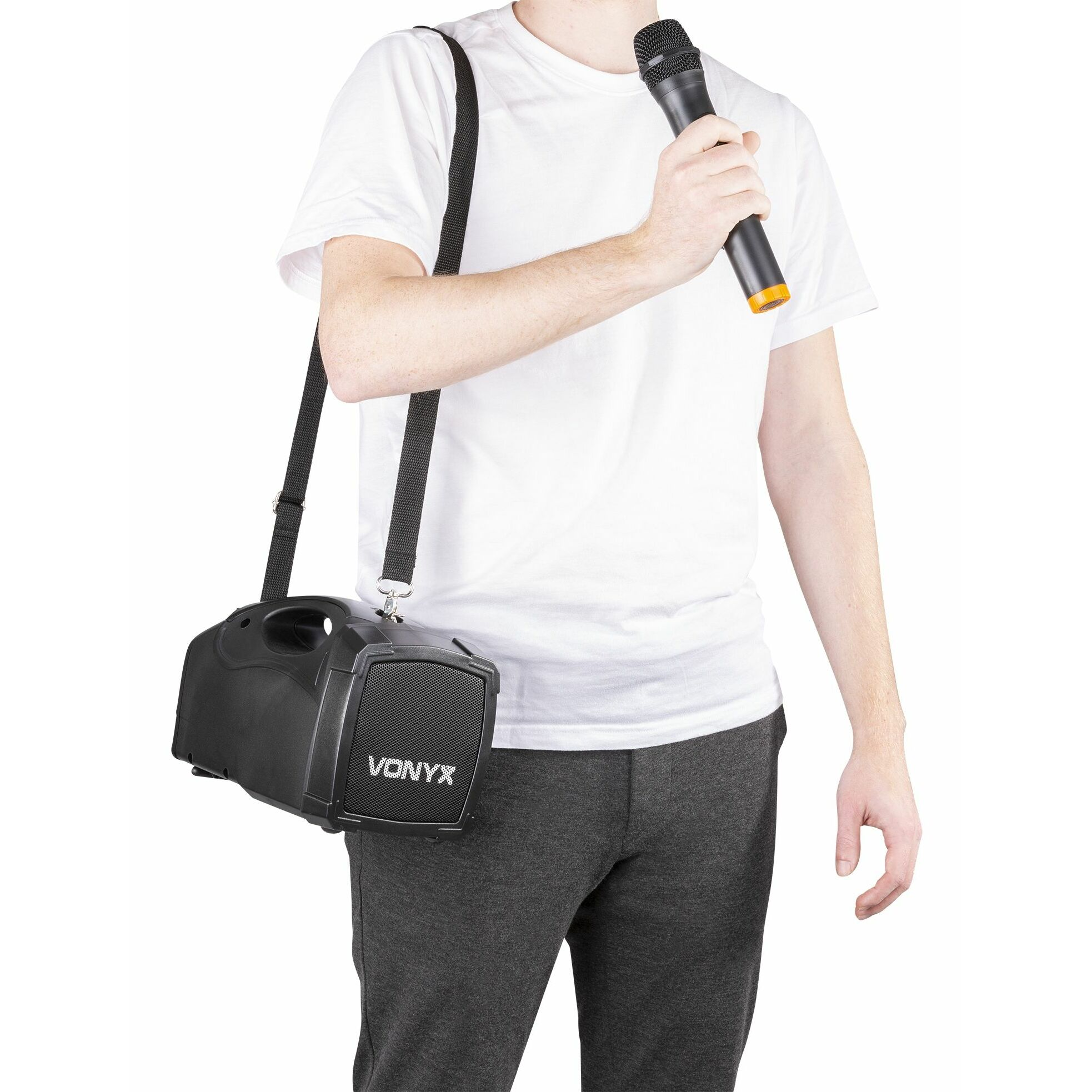 Hombre con altavoz Vonyx negro en el hombro y sosteniendo un micrófono. Camisa blanca y pantalón gris.