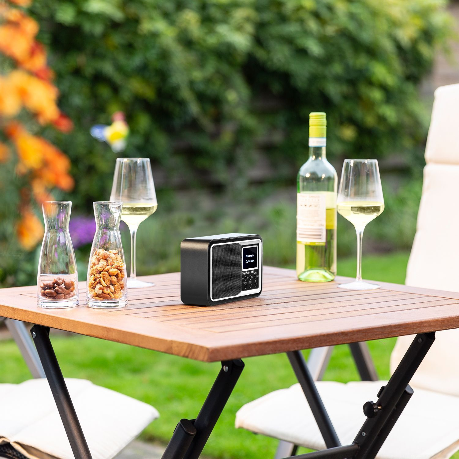 Tisch mit Radio, zwei Weingläsern, einer Flasche Wein und zwei kleinen Gläsern mit Snacks.