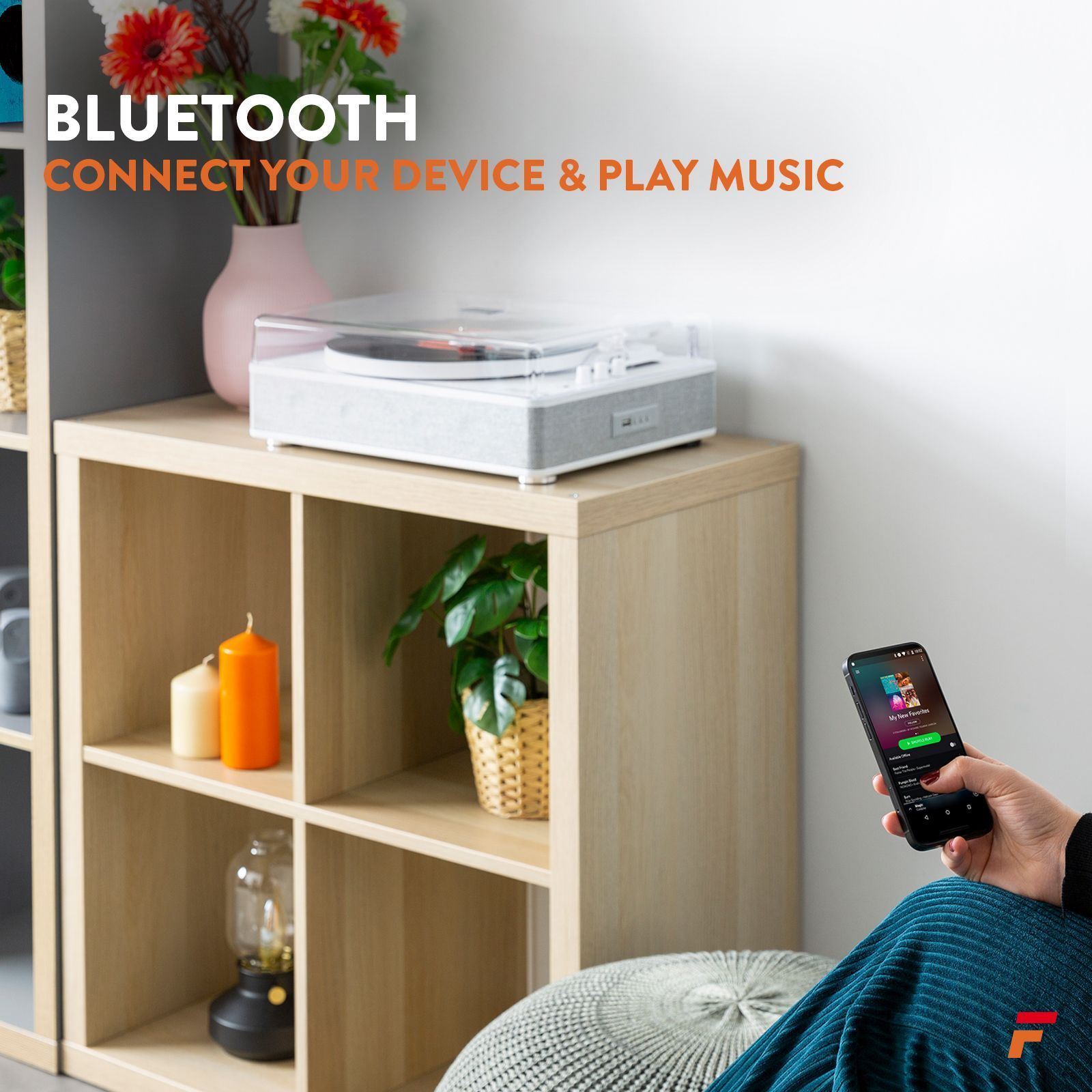 Eine Person hört Musik auf ihrem Telefon. Ein Plattenspieler und Lautsprecher stehen im Hintergrund auf einem Holzregal.