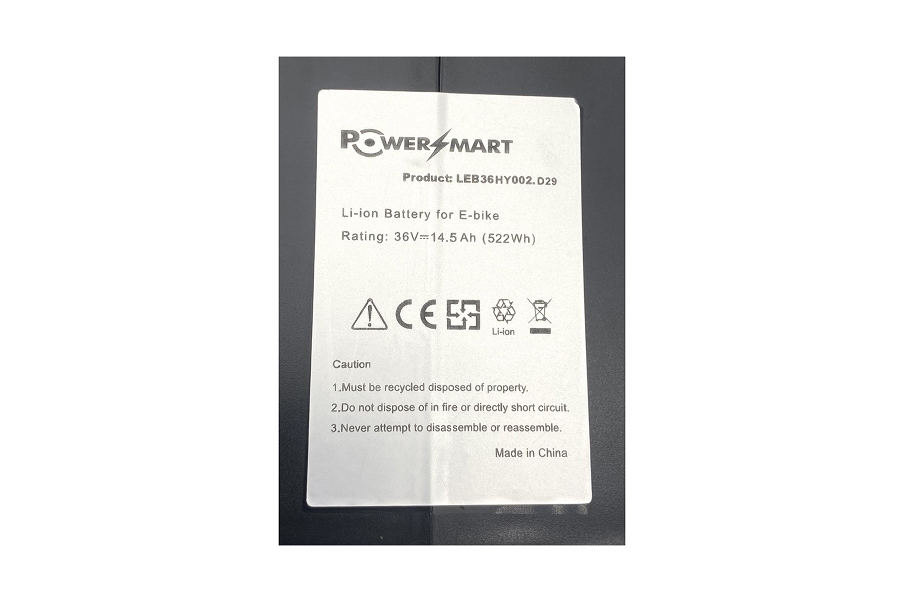 Weißes Etikett mit Text, Warnhinweisen und einem Logo. Es ist eine Li-Ionen-Batterie für E-Bikes.