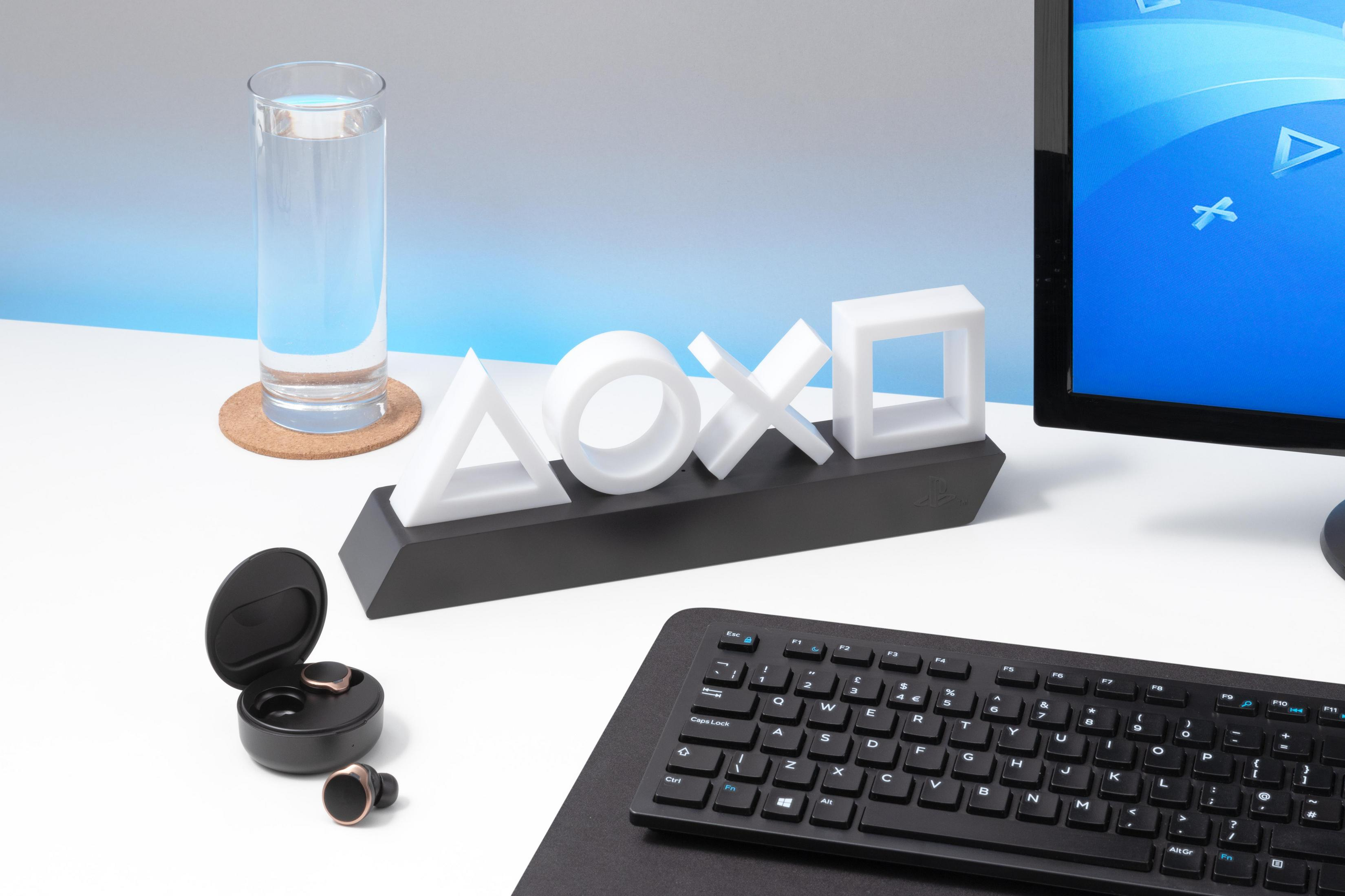 Schreibtisch mit PS-Symbolleuchte, Monitor, Tastatur, Glas Wasser und Kopfhörern.