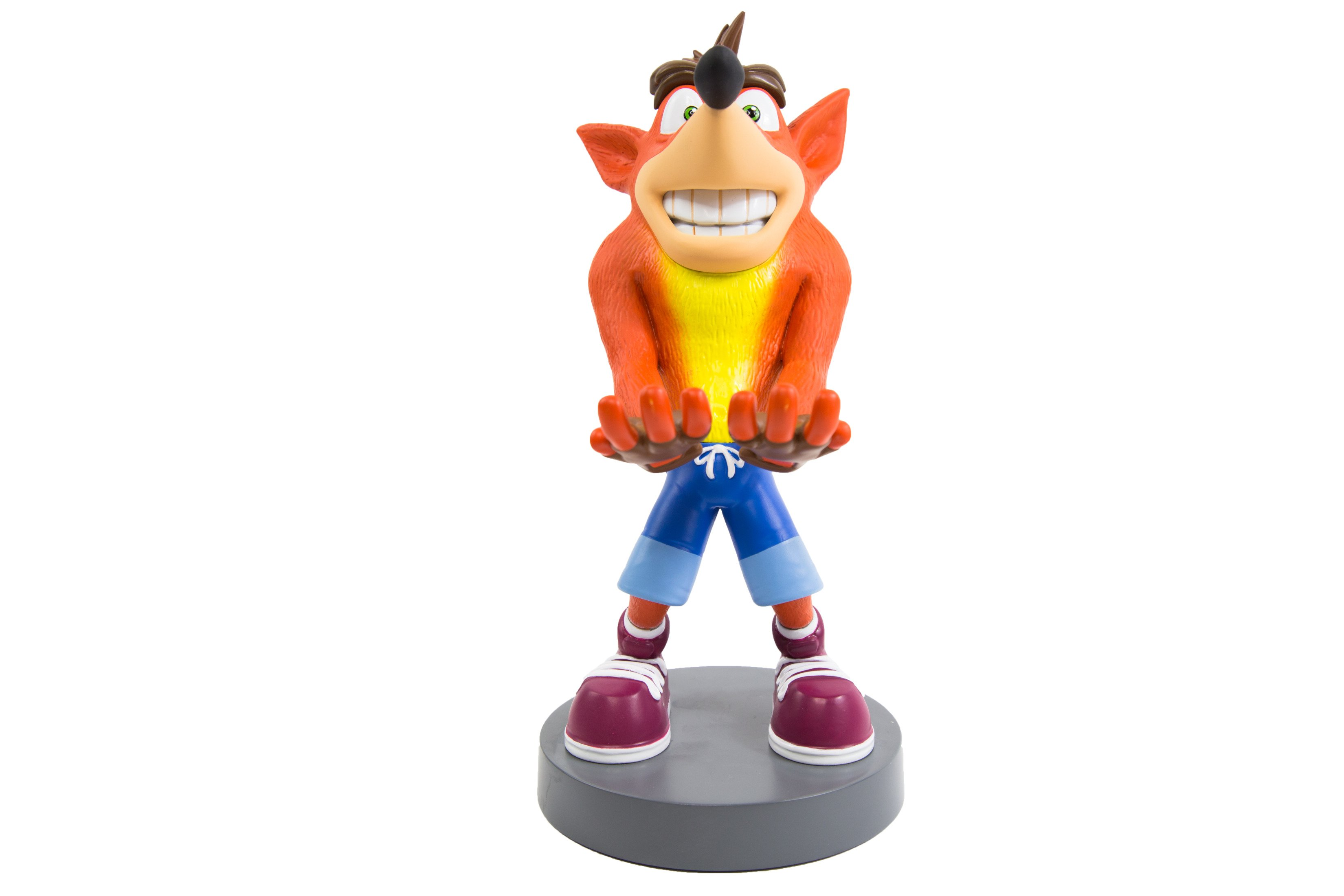 Figurina di Crash Bandicoot, pelliccia arancione, pancia gialla, pantaloncini blu, su base grigia, sfondo bianco.