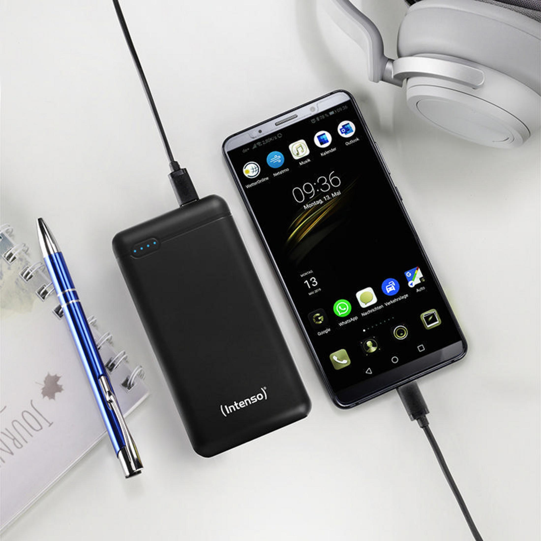 Ein Telefon, das neben einer Powerbank, einem Stift und einem Notizbuch geladen wird. Der Hintergrund ist ein weißer Schreibtisch.