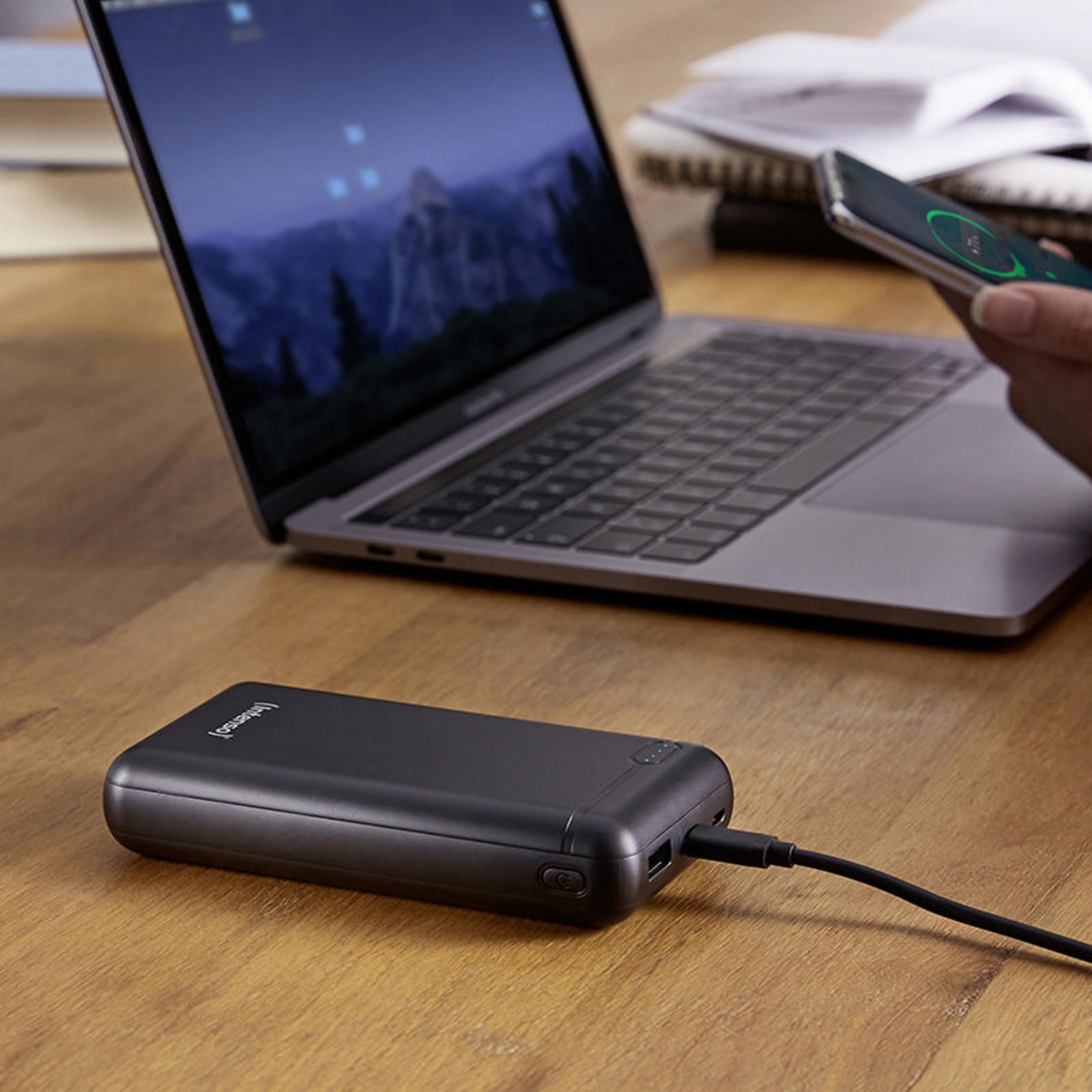 Schwarze Powerbank, verbunden mit Laptop und Smartphone, auf Holztisch.