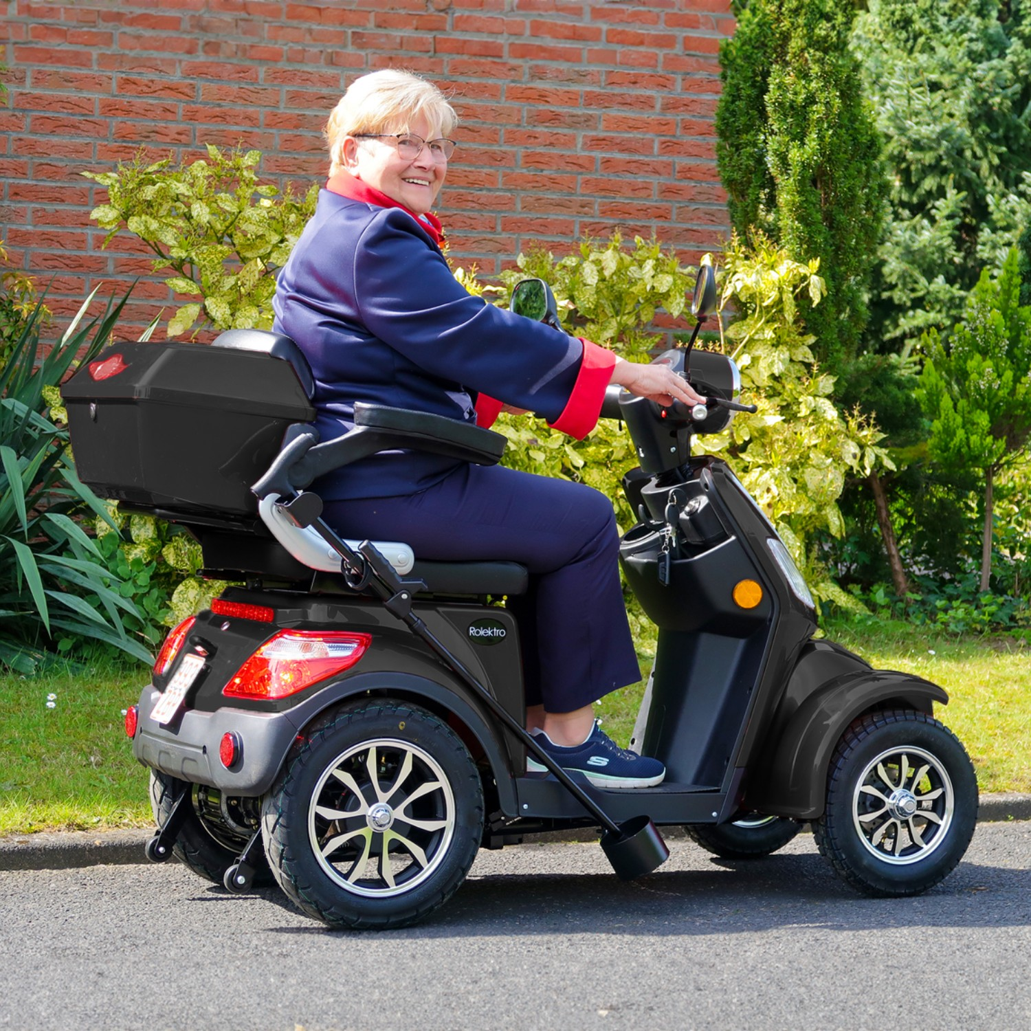 Eine ältere Frau fährt an einem sonnigen Tag mit einem schwarzen Elektromobil.