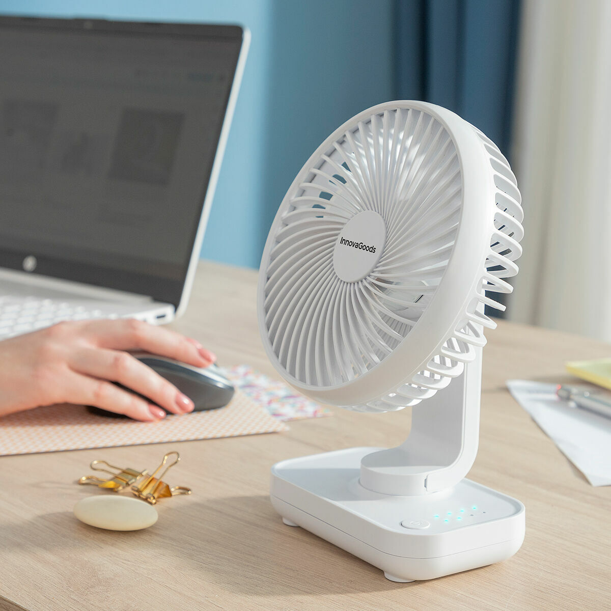 Ventilador de escritorio blanco con portátil y mano de persona cerca.