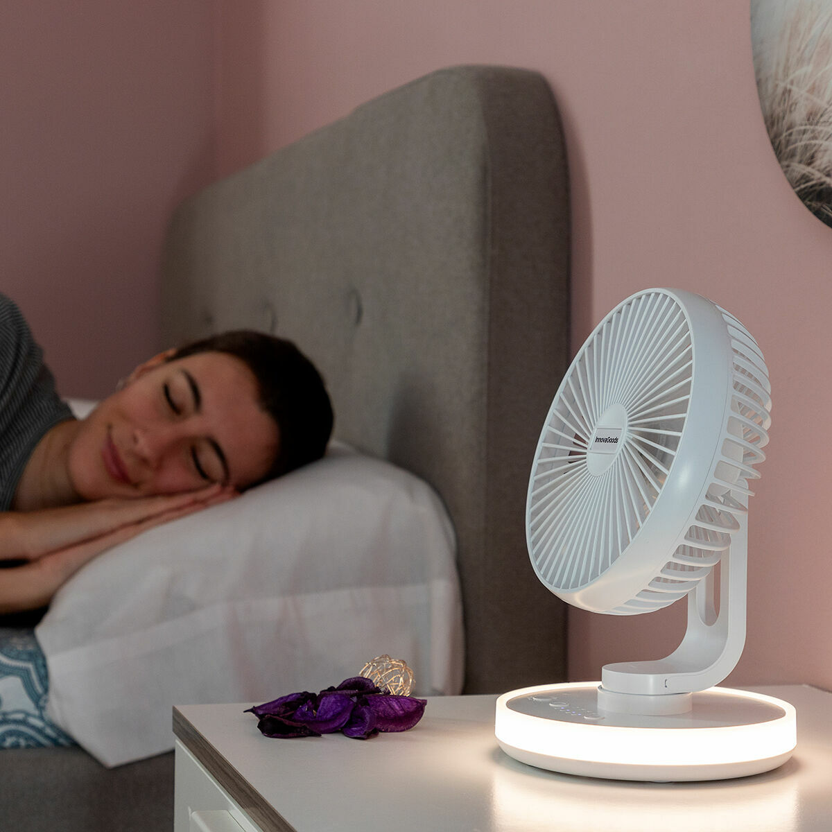 Frau schläft im Bett neben einem weißen Nachttischventilator. Der Ventilator hat ein Licht.