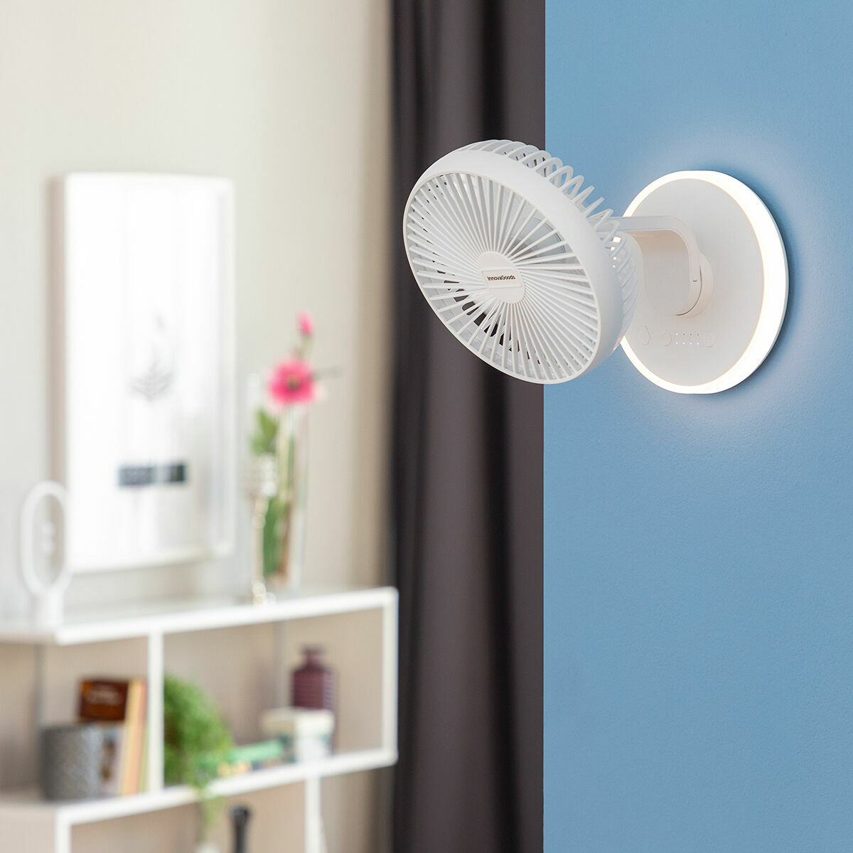 Ein weißer Wandventilator mit einem kreisförmigen Licht an einer blauen Wand. Ein kleines Regal ist im Hintergrund.