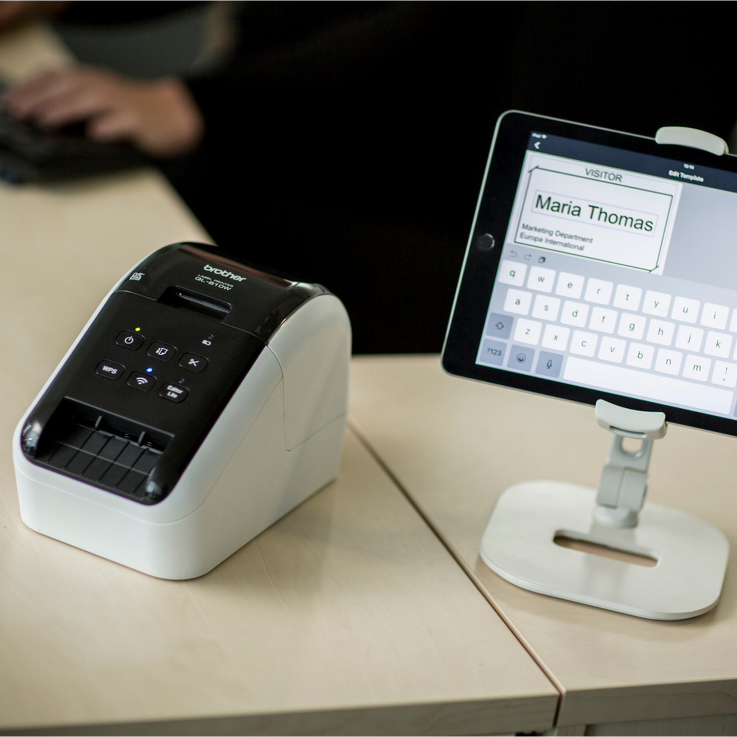 Label printer next to a tablet displaying a visitor form. A person is using the tablet.