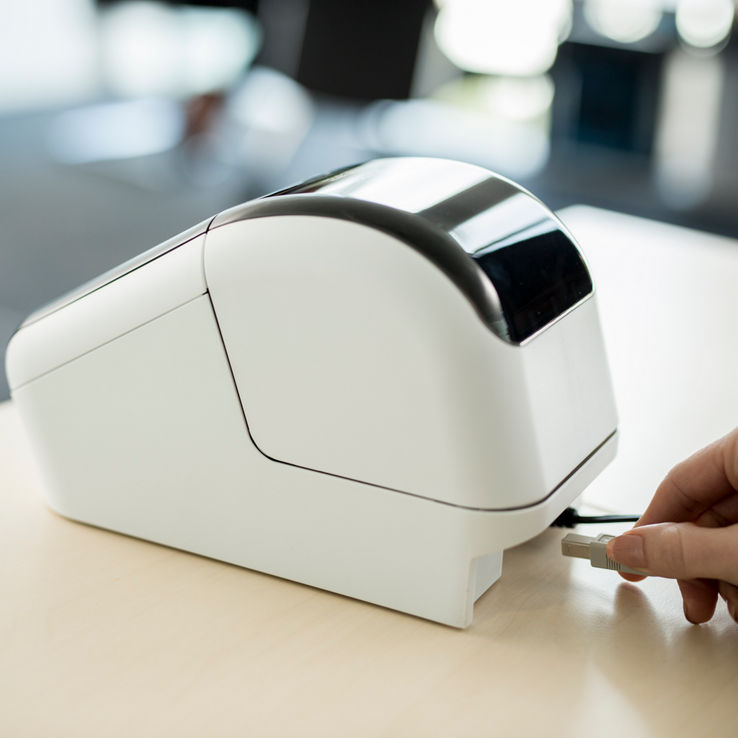 A hand plugging in a USB cable into a label printer.