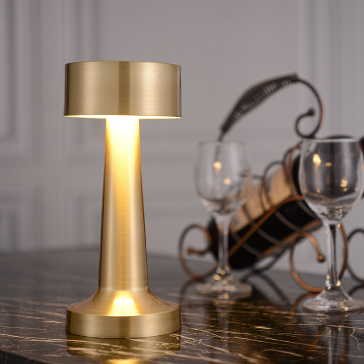 Goldene Lampe auf einem Tisch. Weingläser und ein Weinregal sind im Hintergrund unscharf.