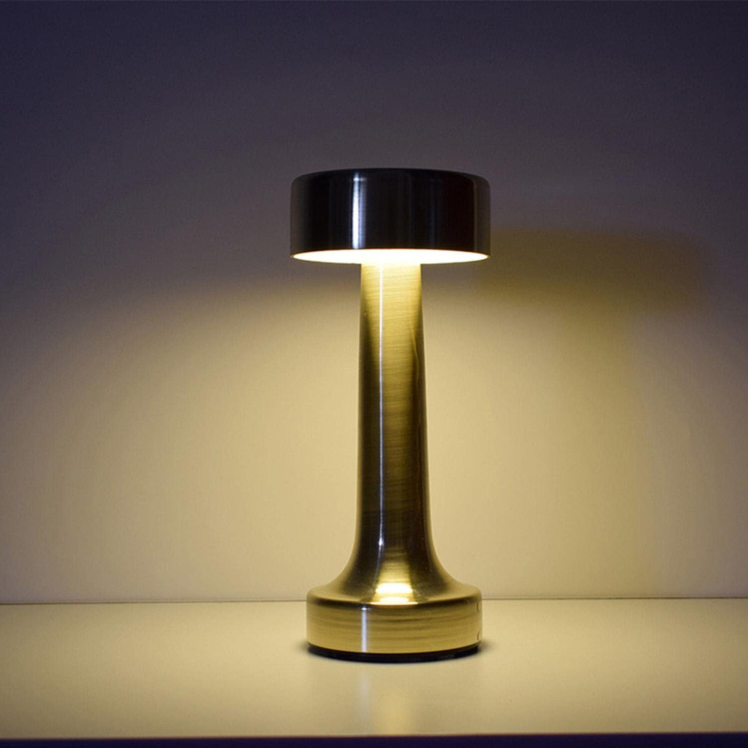 Messingfarbene Lampe mit zylindrischem Kopf, langem Stiel und rundem Fuß, eingeschaltet.