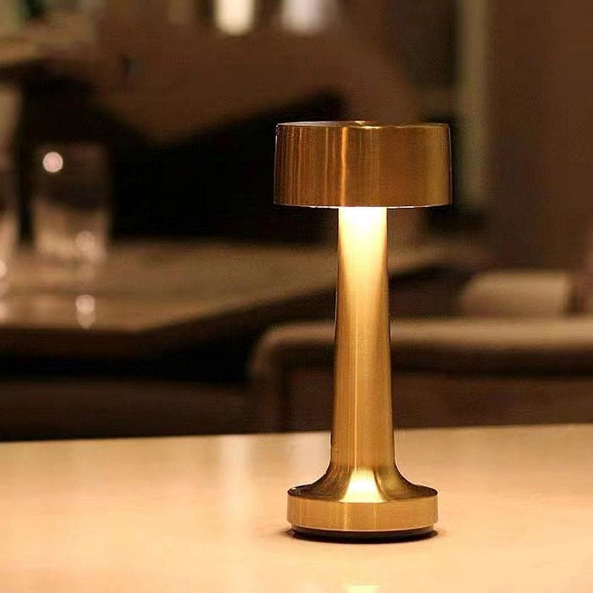 Goldfarbene Tischlampe mit zylindrischem Fuß und Schirm, die warmes Licht ausstrahlt.